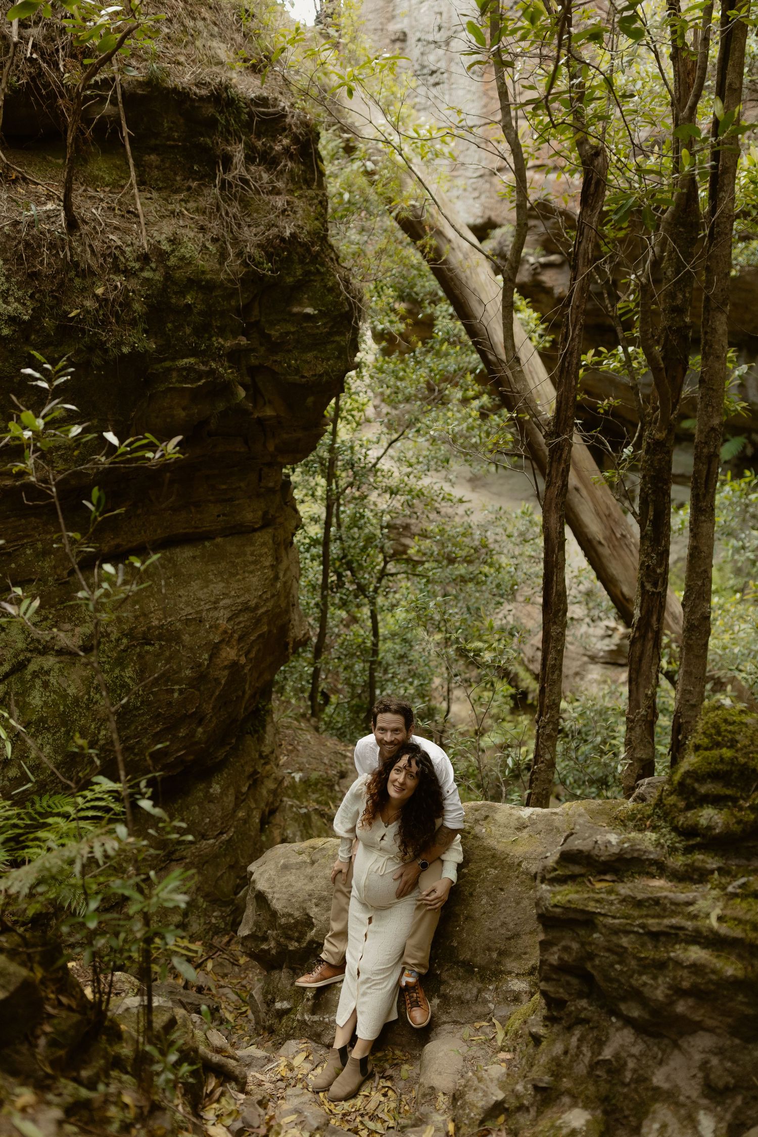 Hikers explore a scenic wooded trail along rocky cliffs and outcroppings in a lush forest setting.