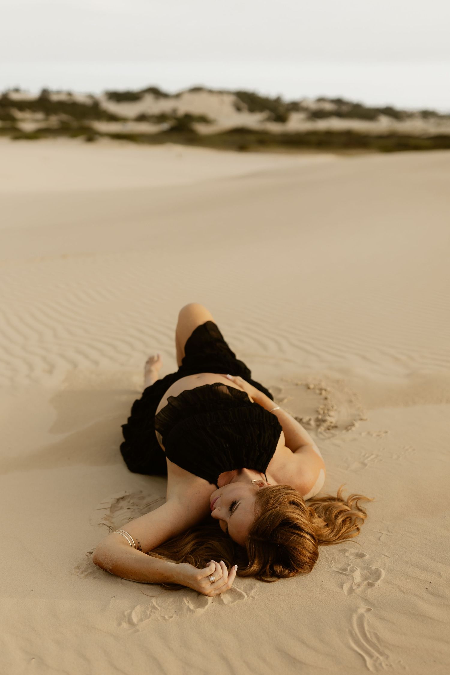 A figure in black clothing lies gracefully on rippled desert sand creating an artistic pose.