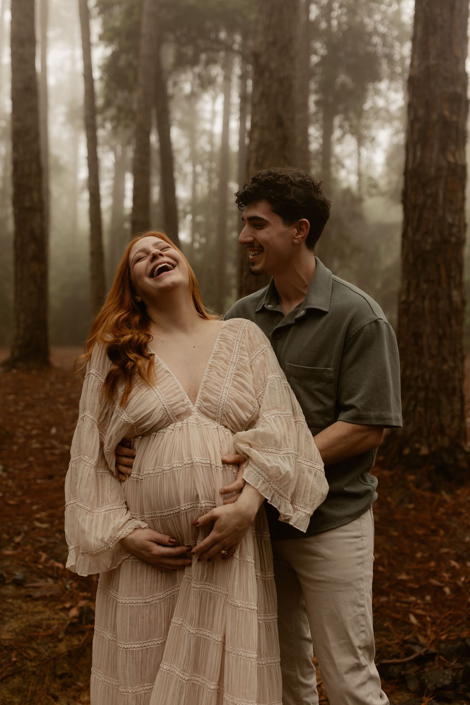An intimate maternity photography session captures tender moments between a couple in a wooded setting.
