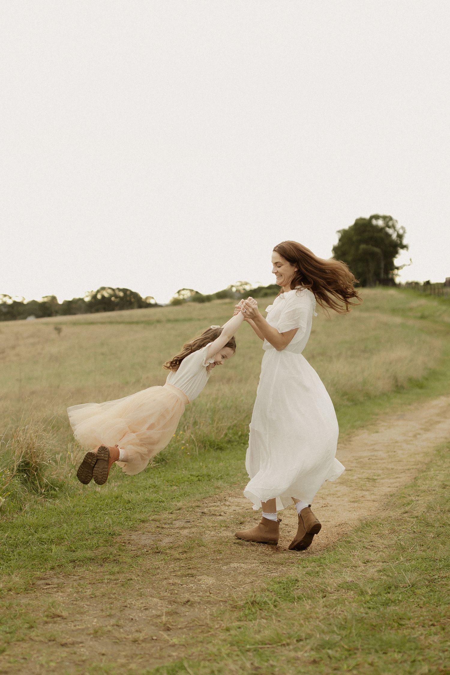 A sequence of dance movements in a white dress and boots across a grassy hillside path.