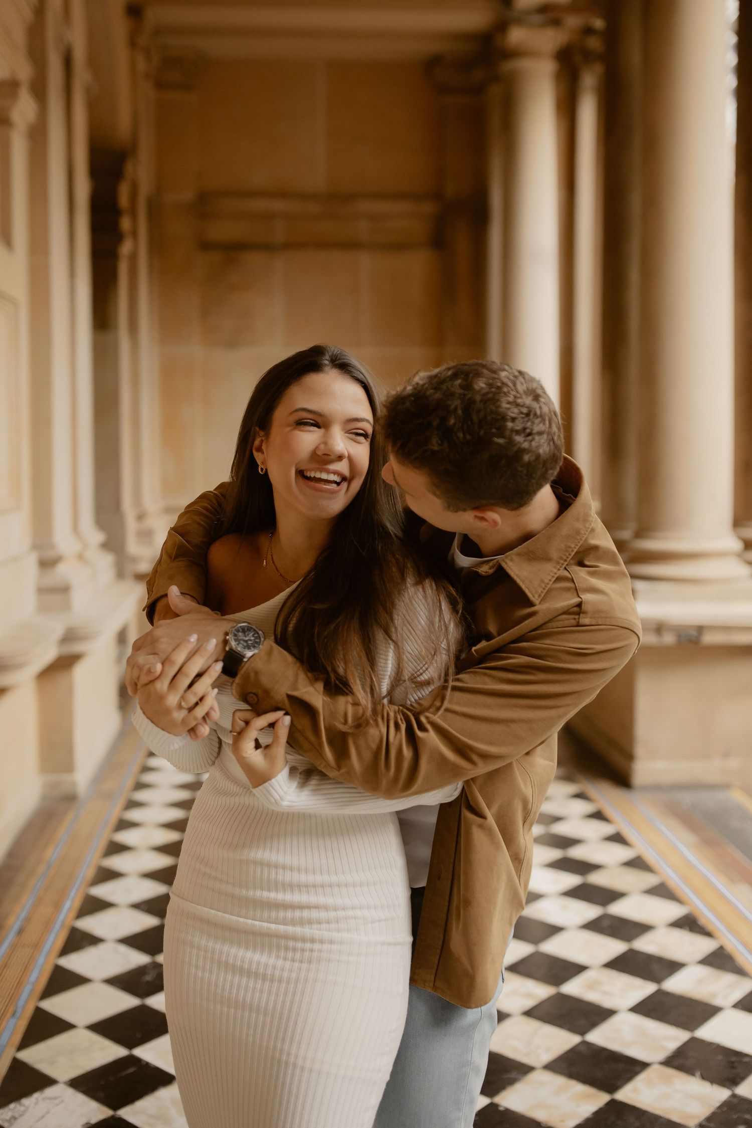 A joyful couple embraces while laughing together in a historic building with ornate architecture.