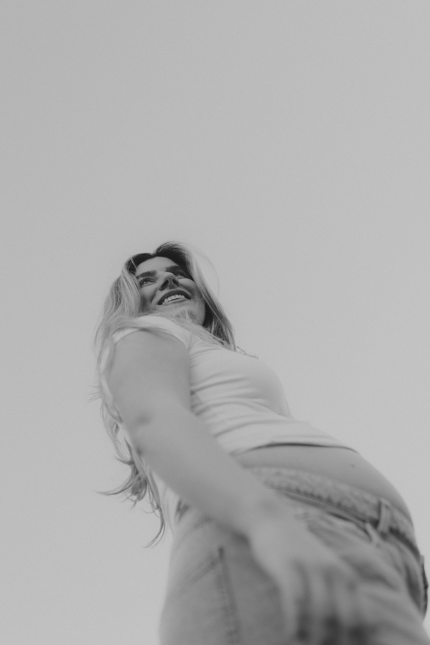 Black and white low angle shot of laughing pregnant woman in white tank top.