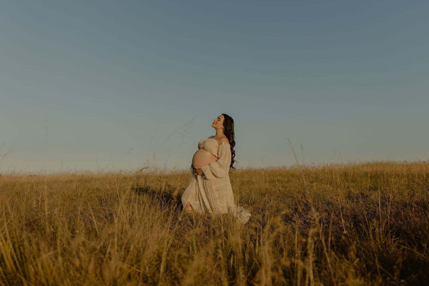 A person in a flowing dress stands in a golden wheat field at sunset creating a dreamy silhouette.