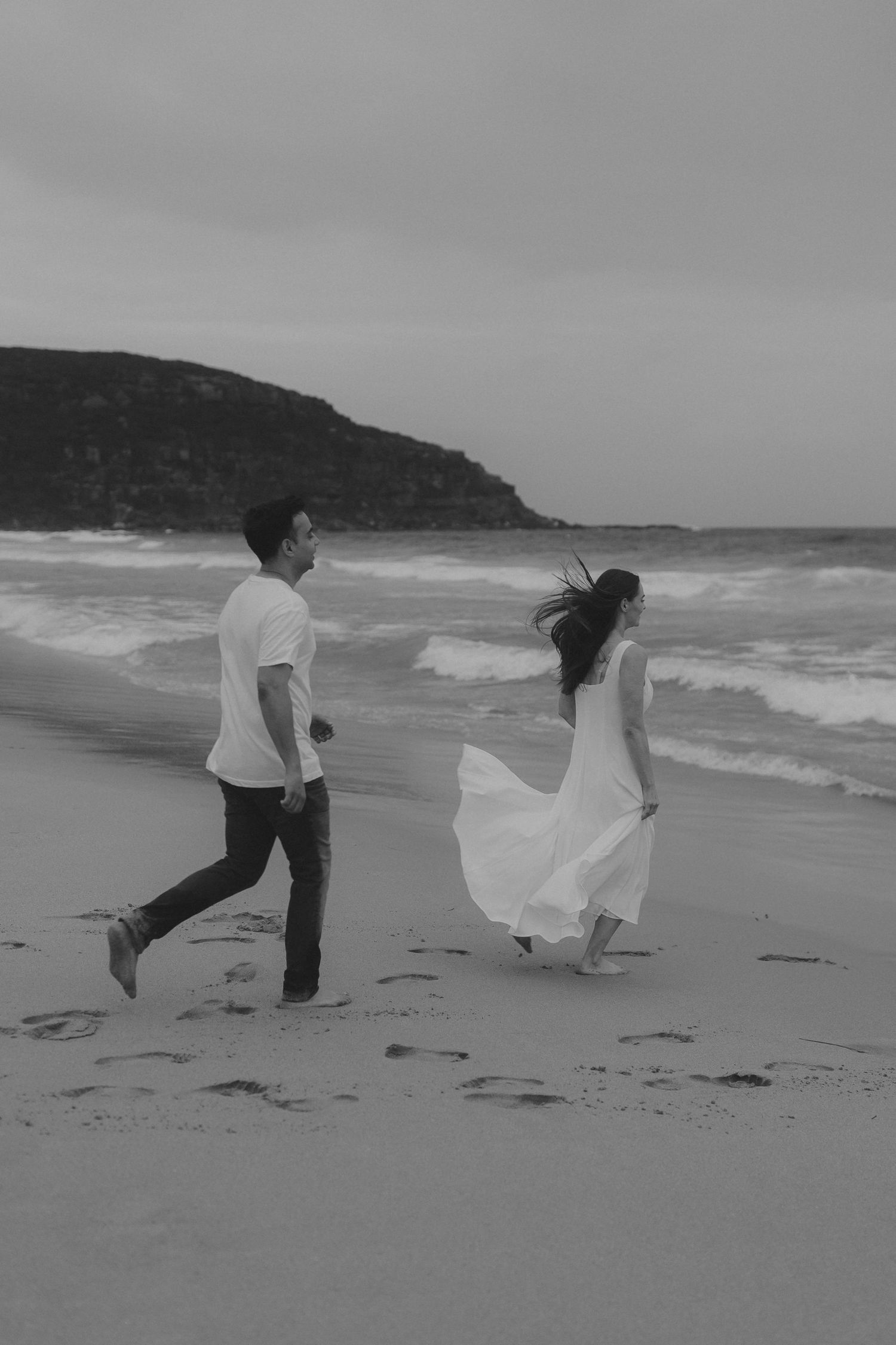 Black and white photos of a couple dancing playfully on a windy beach with flowing white fabric.