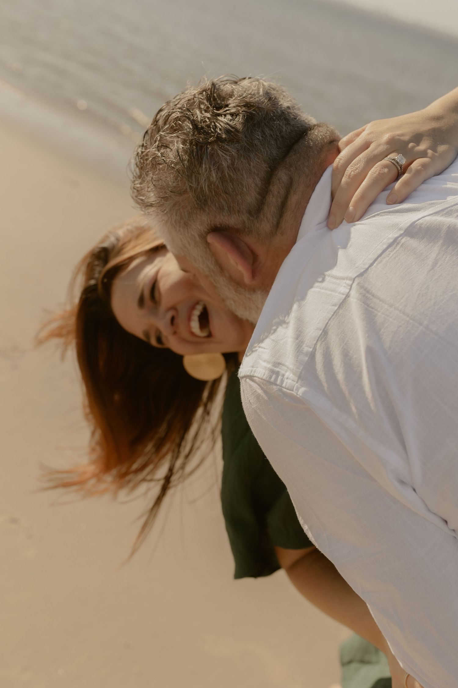 Person in white shirt laughing and dancing playfully on a beach during sunset.
