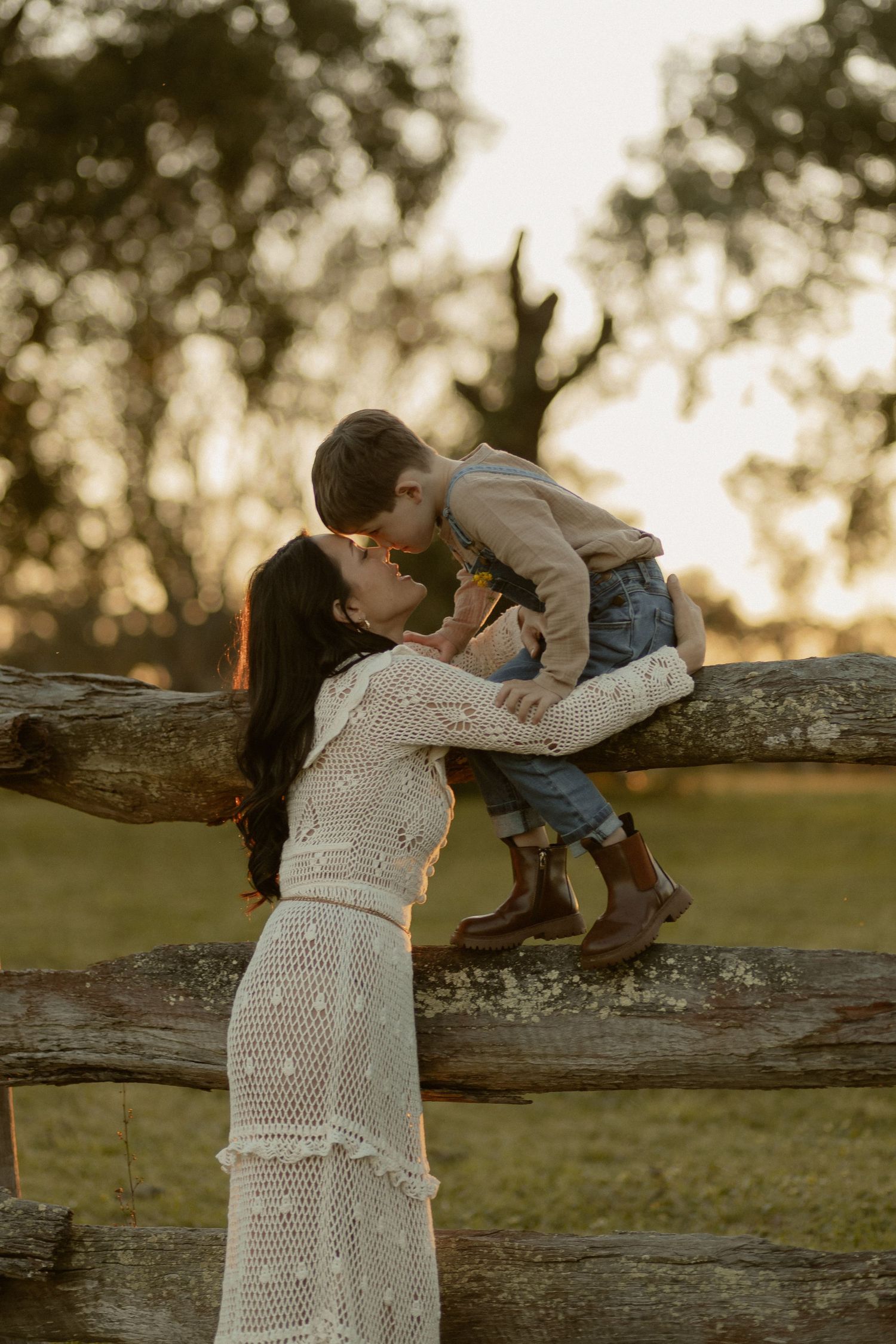 A family shares intimate moments by a wooden fence during golden hour.