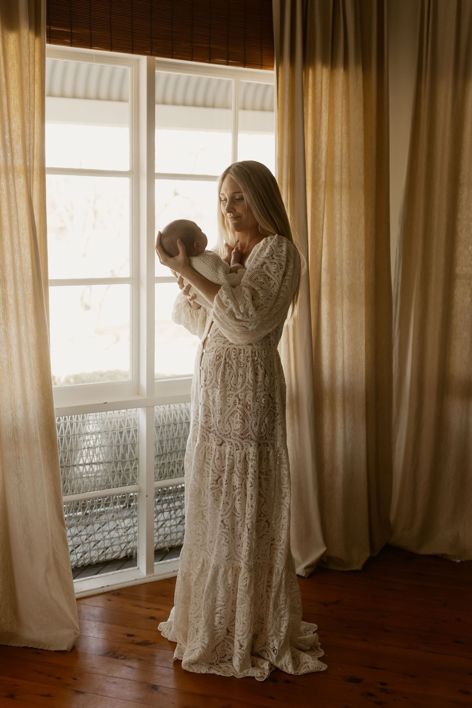 A person in a white lace dress twirls gracefully in front of sunlit windows creating a dreamy silhouette.