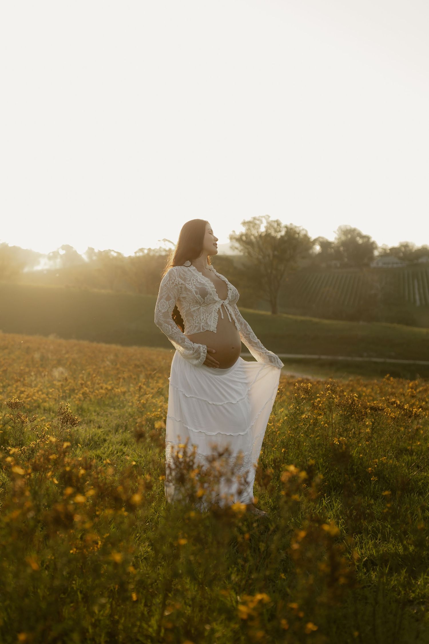 Two figures in flowing white dresses dance through a sunlit wildflower meadow at golden hour.