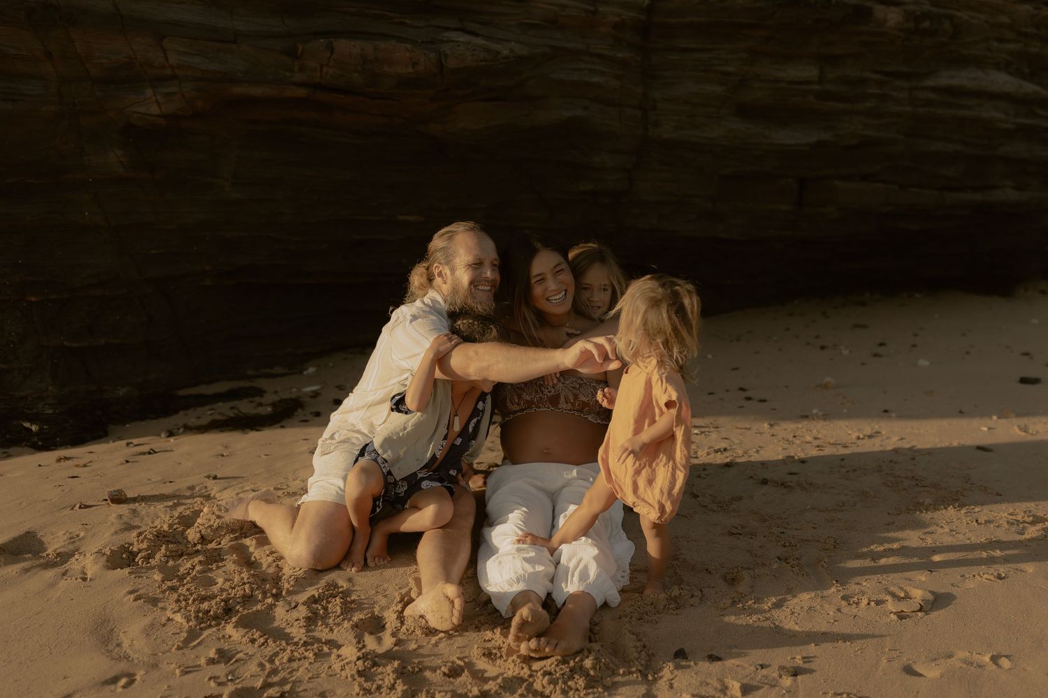 A couple shares an intimate moment while sitting on a sandy beach at sunset.