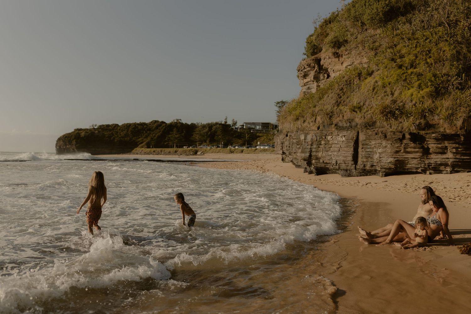People enjoying a sunny day at a scenic beach with dramatic cliffs and rolling waves along the coastline.