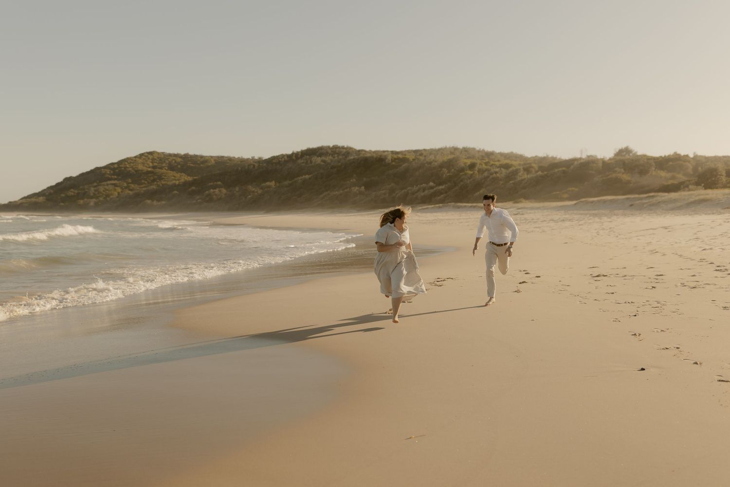 People walking along a scenic beach shoreline at sunset with golden light reflecting off the sand and water.