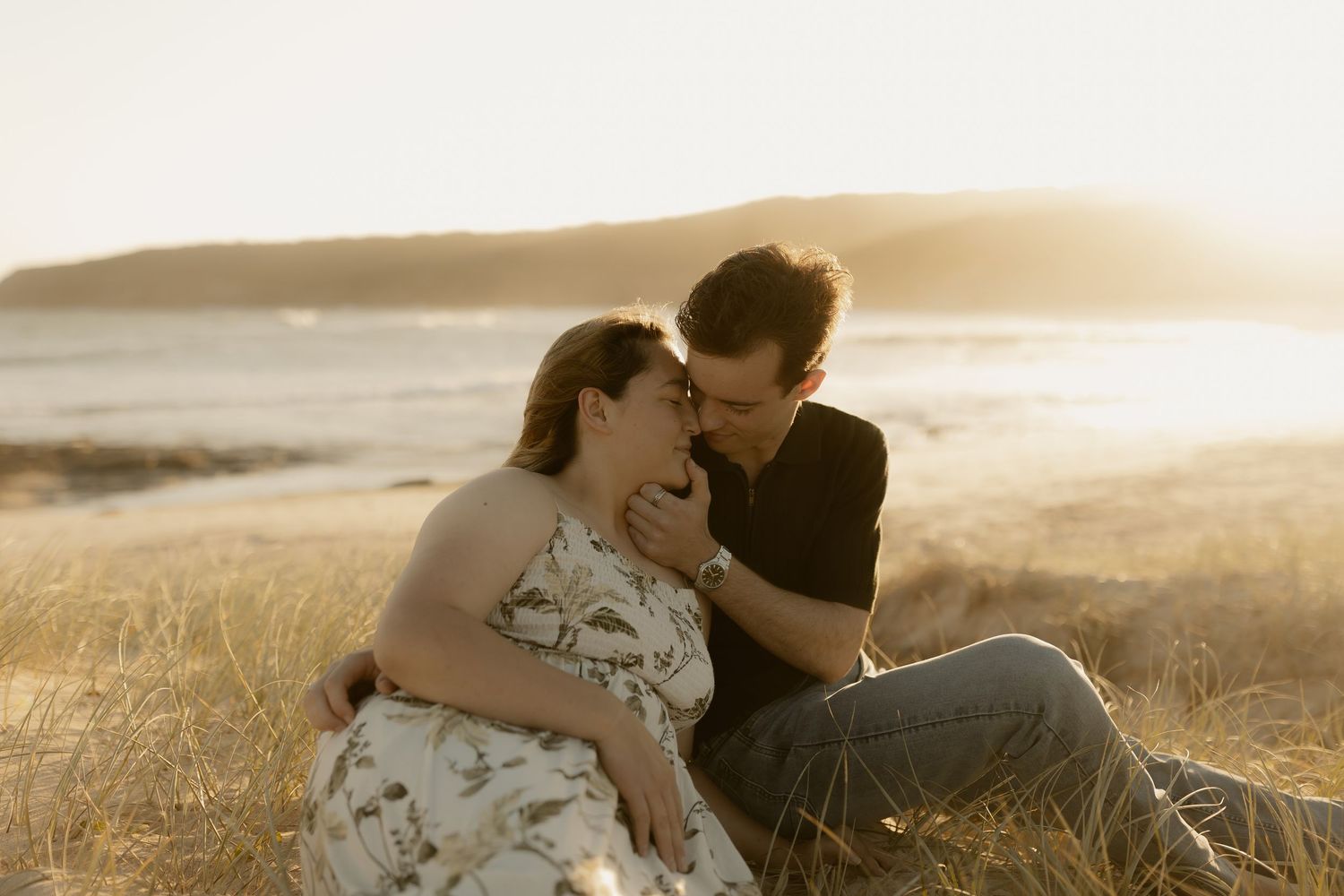 Romantic couple embraces in golden sunlit field during sunset photoshoot.