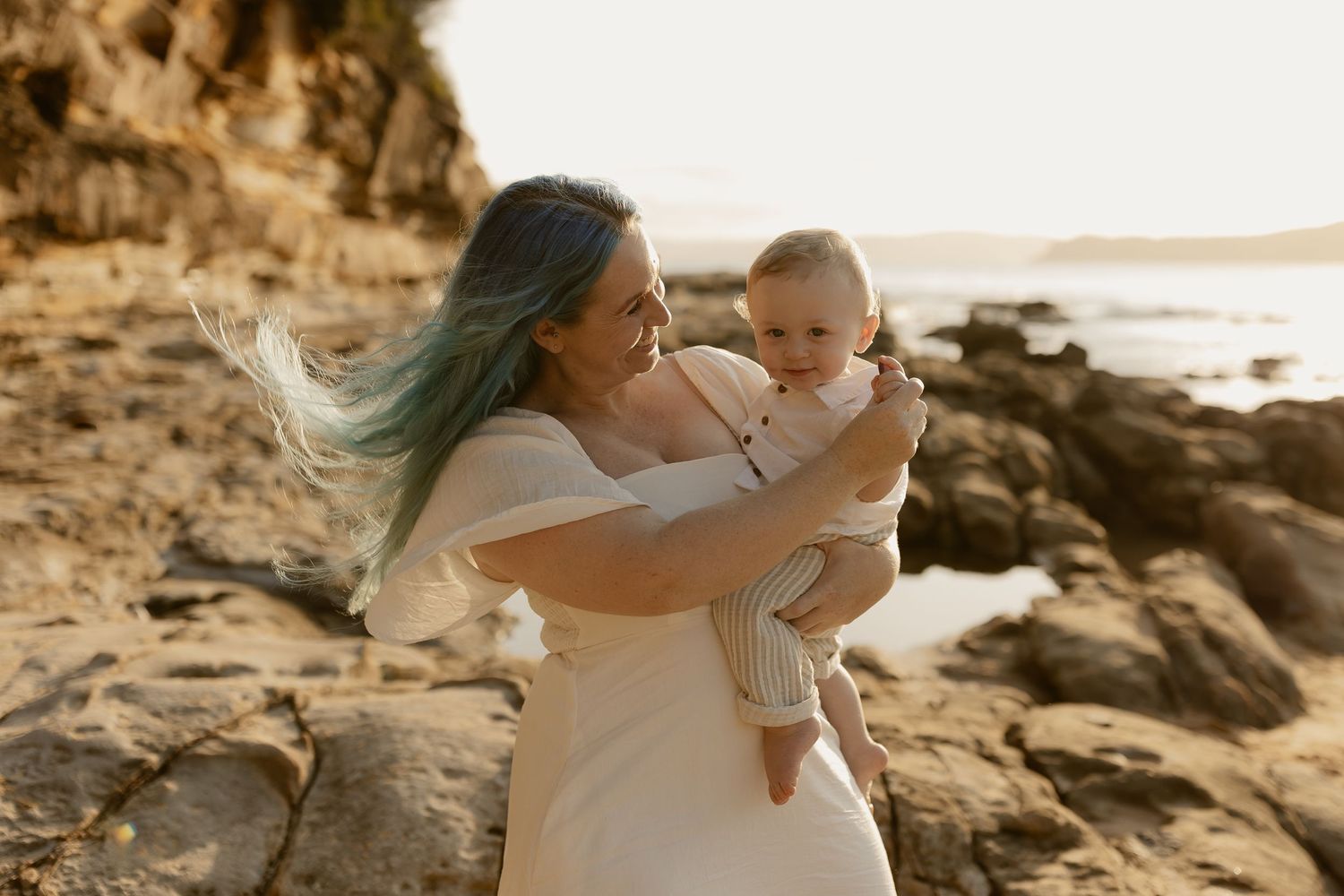 A couple shares intimate moments on a rocky beach at sunset with warm golden light illuminating the scene.