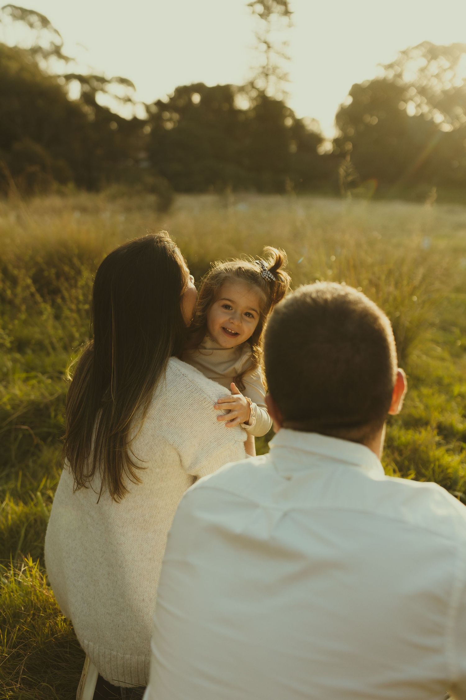A heartwarming family scene unfolds in a golden-lit meadow at sunset.