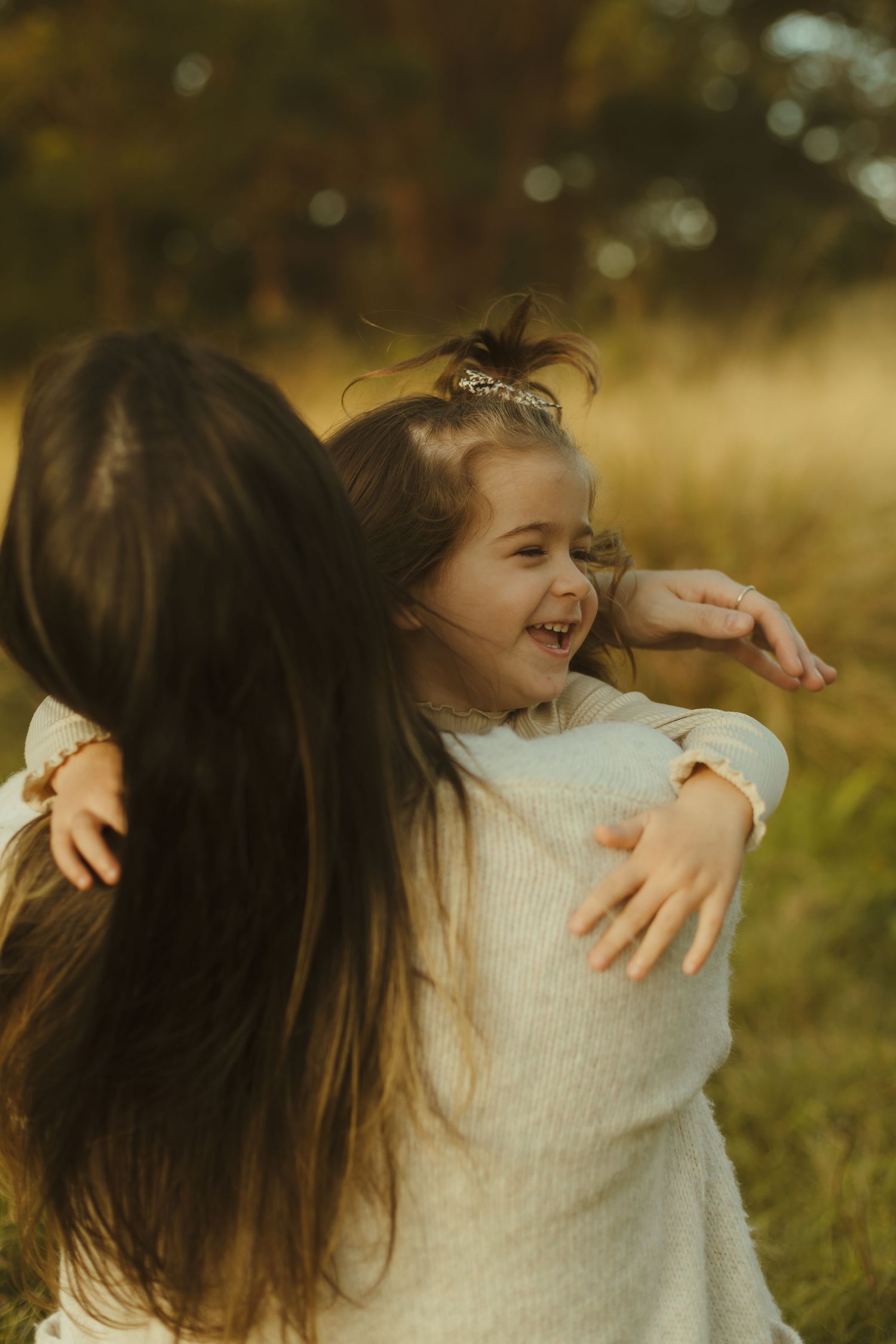 Two people in white sweaters sharing joyful embrace outdoors in warm sunlight.