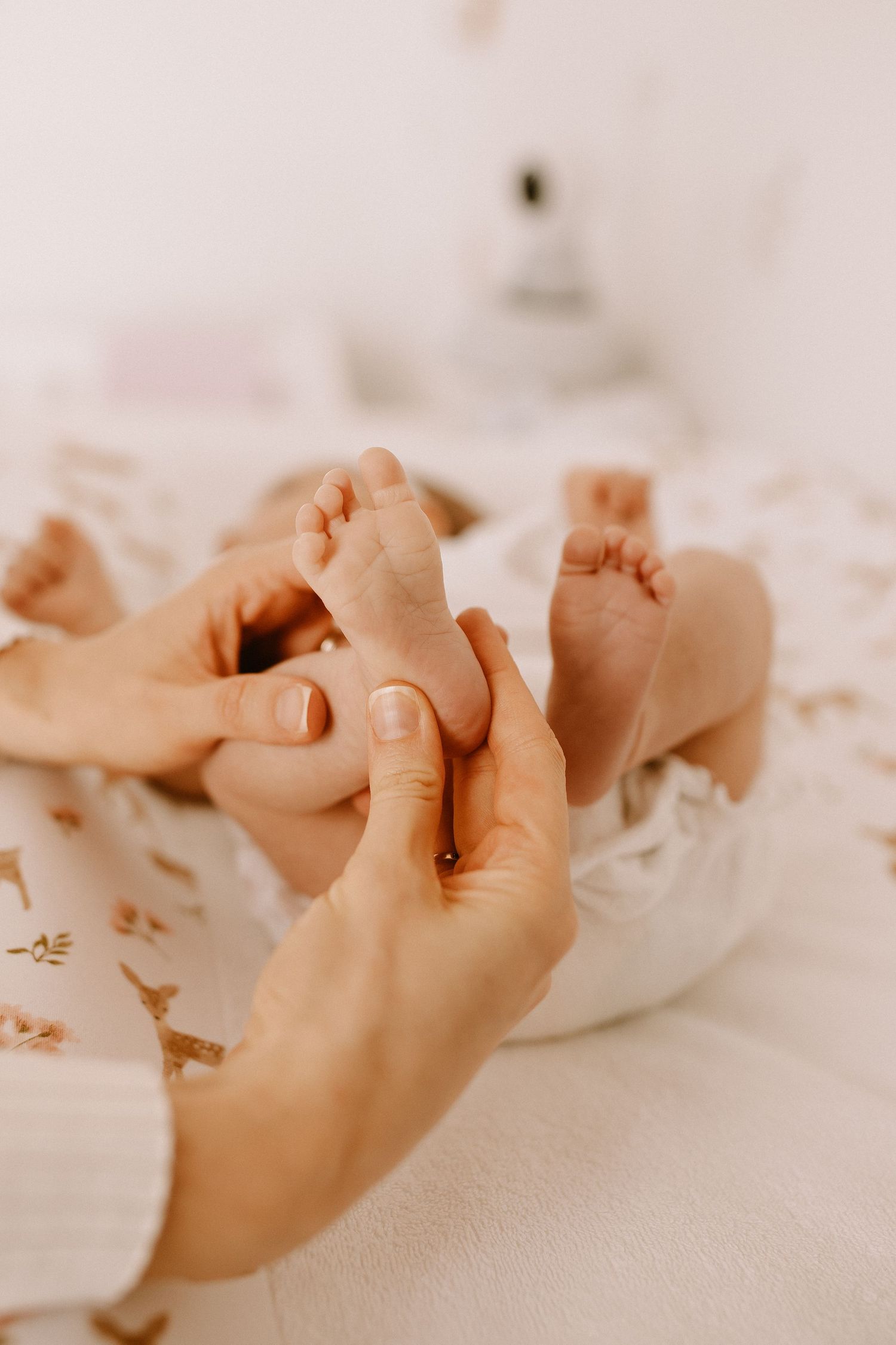 Gentle hands giving a baby foot massage on a white surface with soft lighting and dreamy atmosphere.