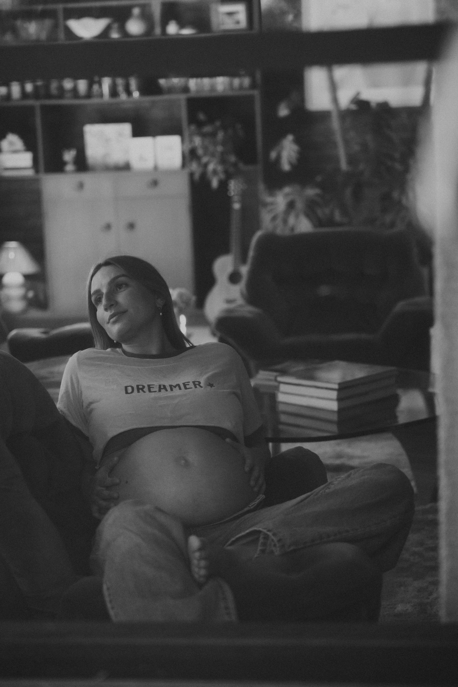 Black and white photo of a pregnant woman in a Dreamer tee reclining on a sofa, holding her bare belly.