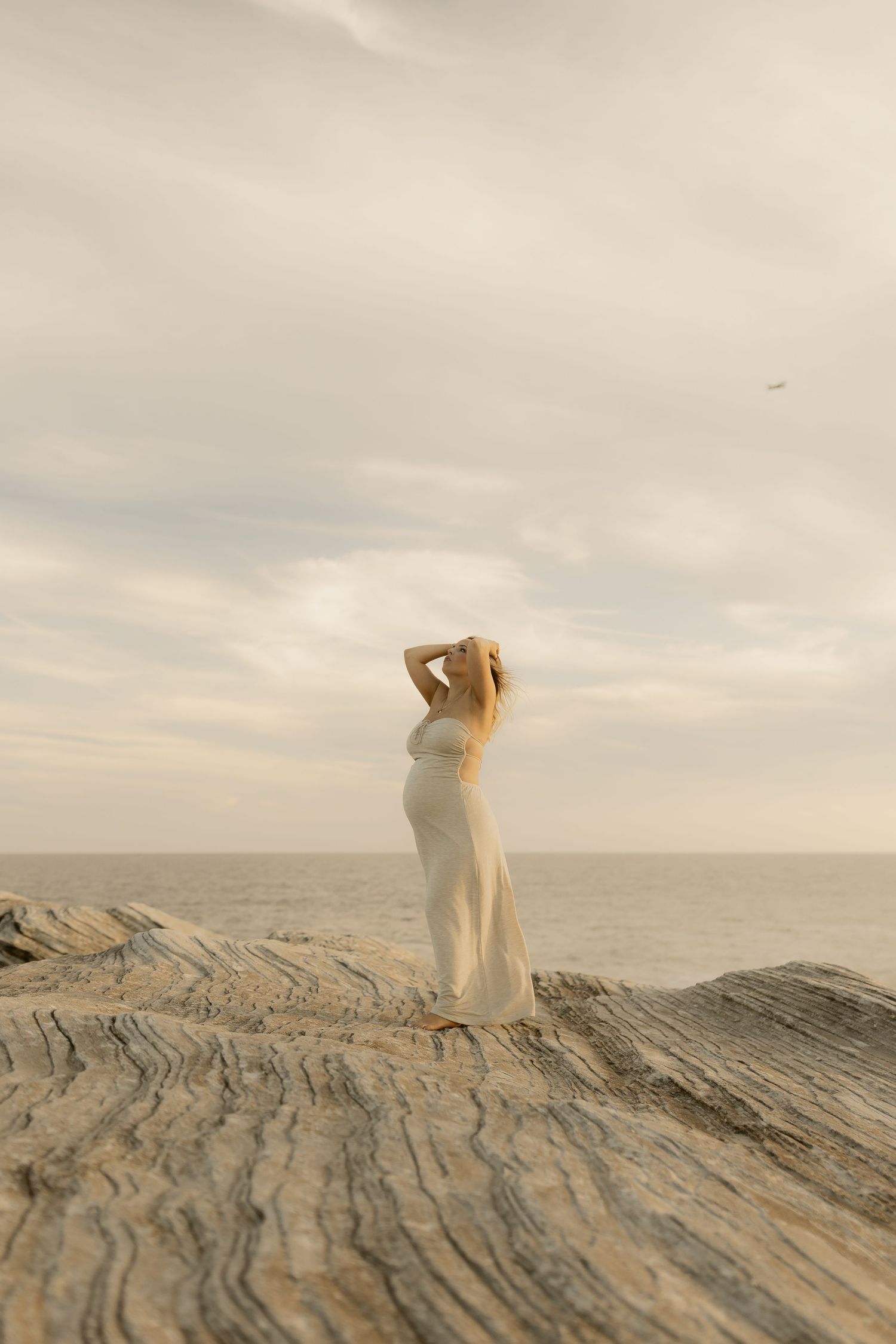 A figure in white stands gracefully atop rugged coastal rocks overlooking the ocean.