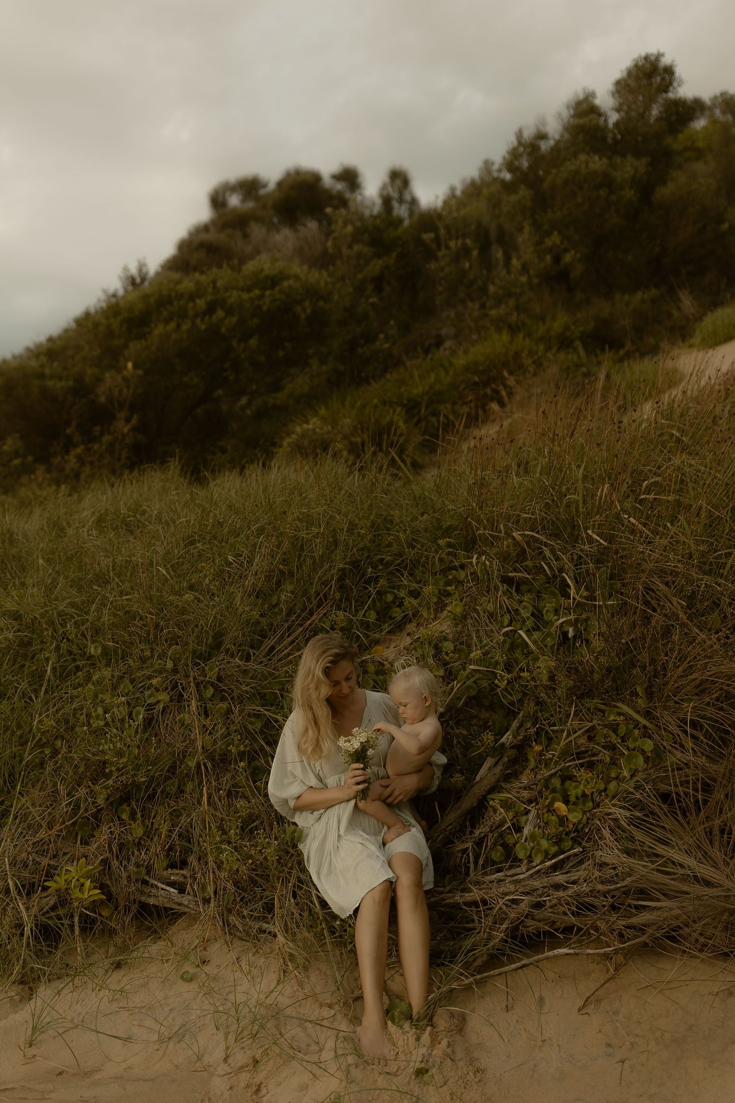 An intimate portrait on sandy dunes with lush greenery and overcast skies in the background.