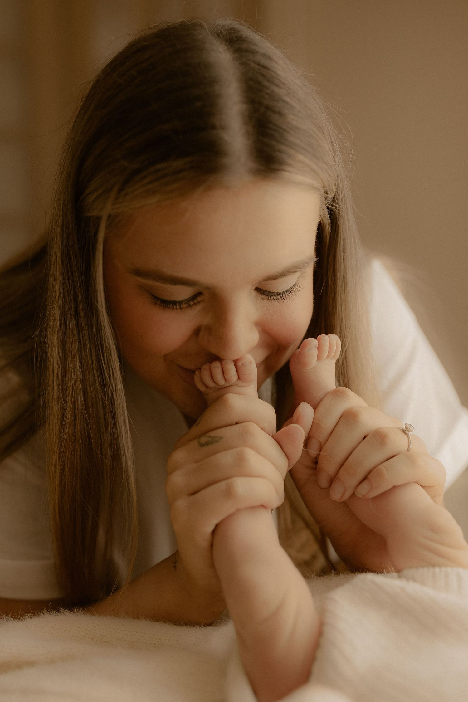 Tender moment as someone kisses tiny baby feet against a warm sepia background.
