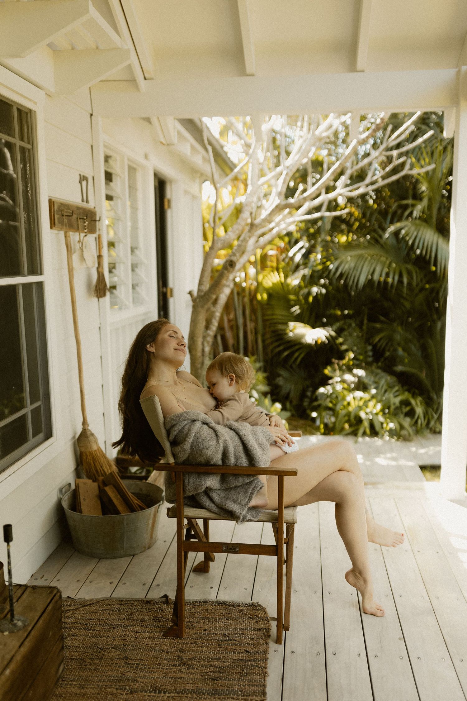 A peaceful moment of bonding on a sunlit wooden porch with wicker furniture and tropical foliage.