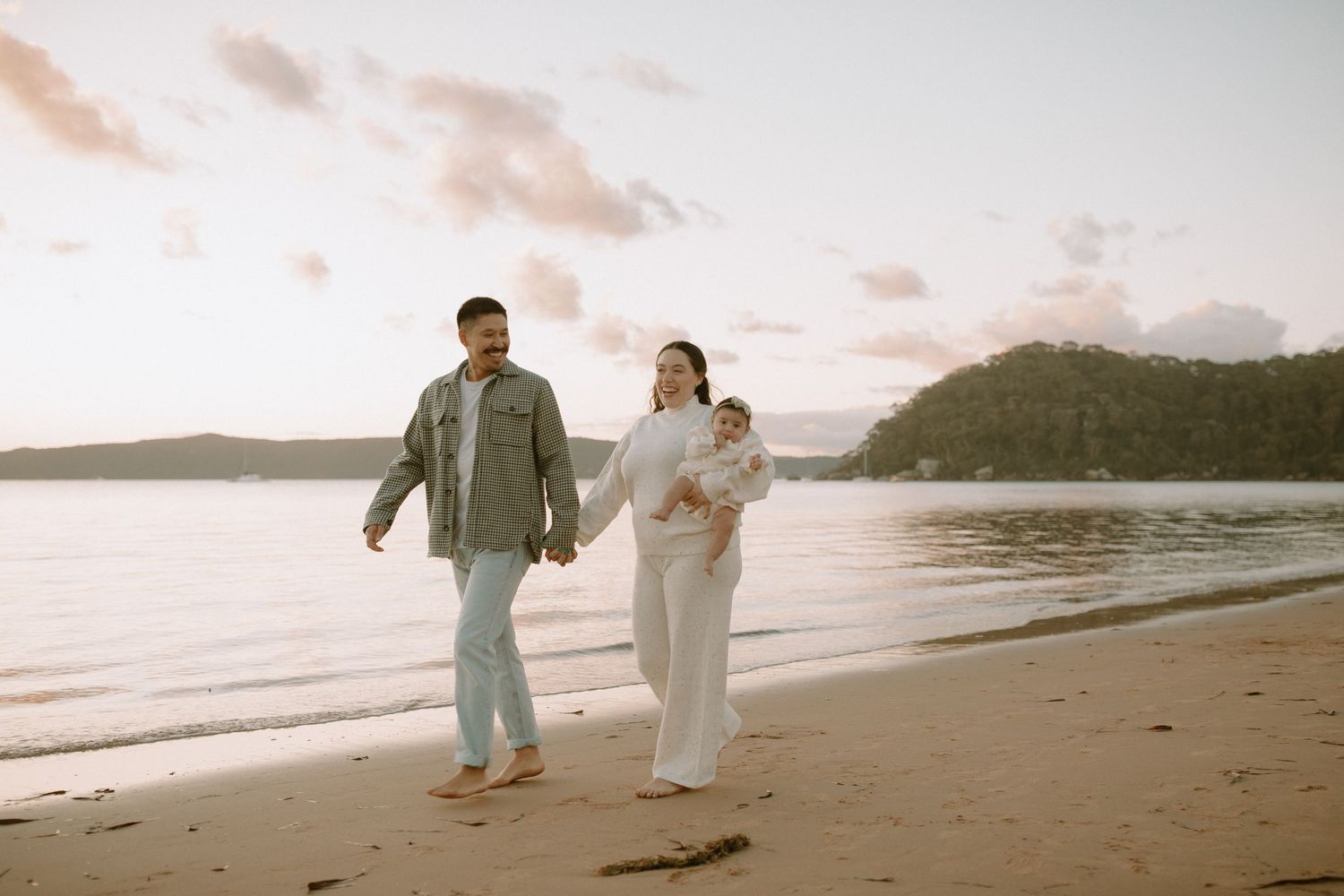 A couple walking hand in hand on a serene beach at sunset with waves rolling onto the shore.