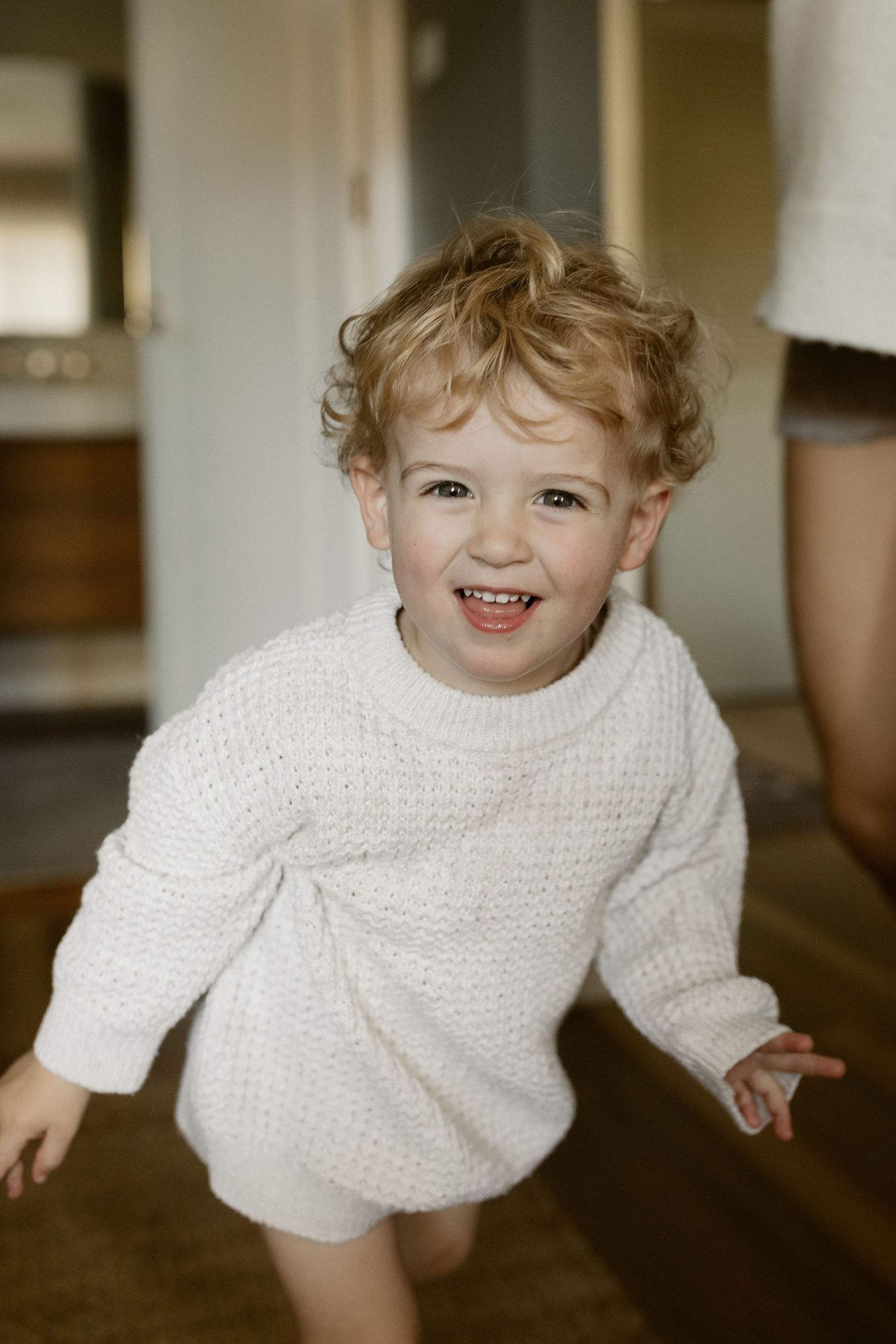 A playful moment captured in warm lighting shows joyful movement in a white knit sweater.