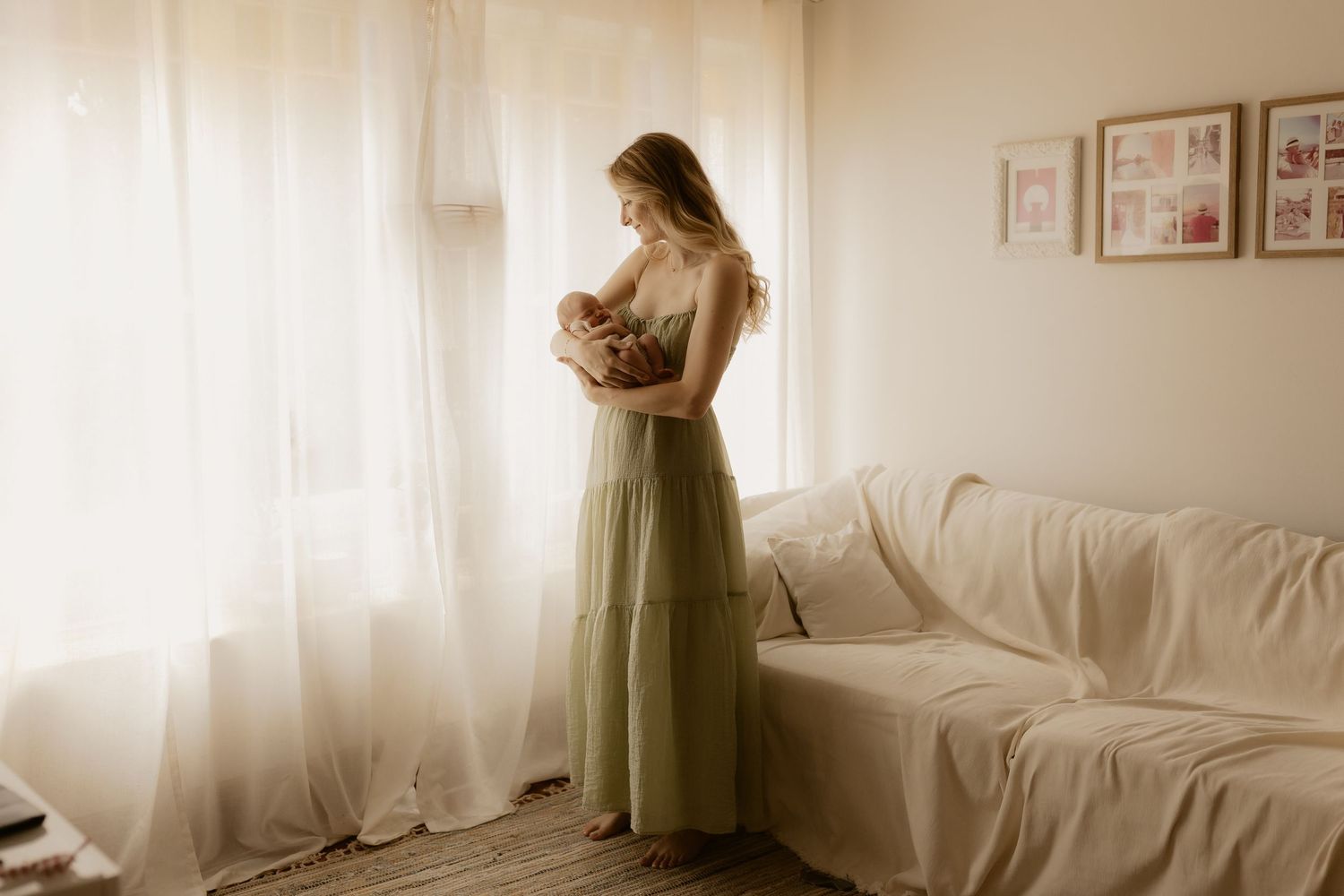 Silhouetted figure in olive green dress stands near sunlit window in minimalist room.