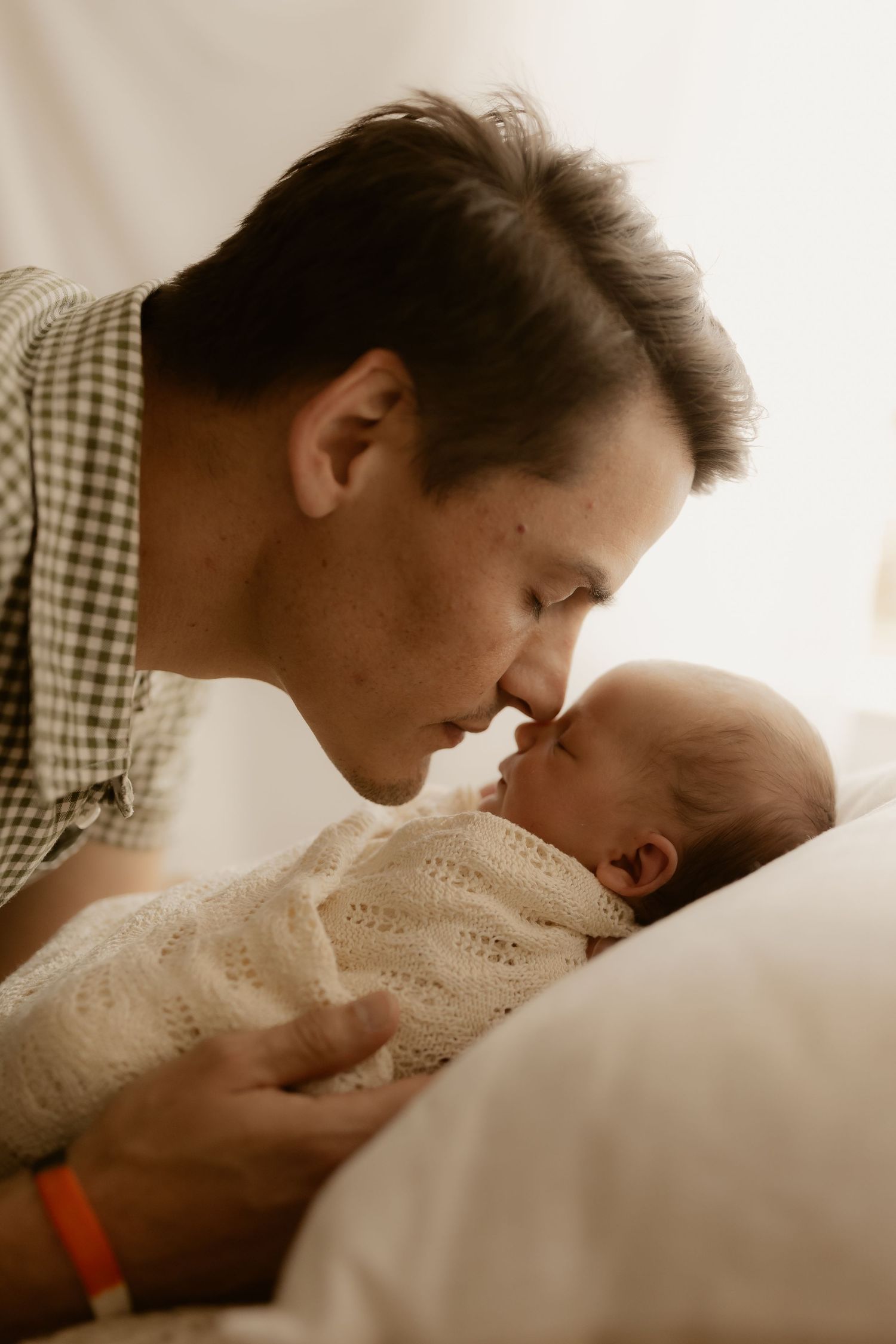 Intimate sepia-toned photo series showing tender moments between parents and newborn in soft lighting.