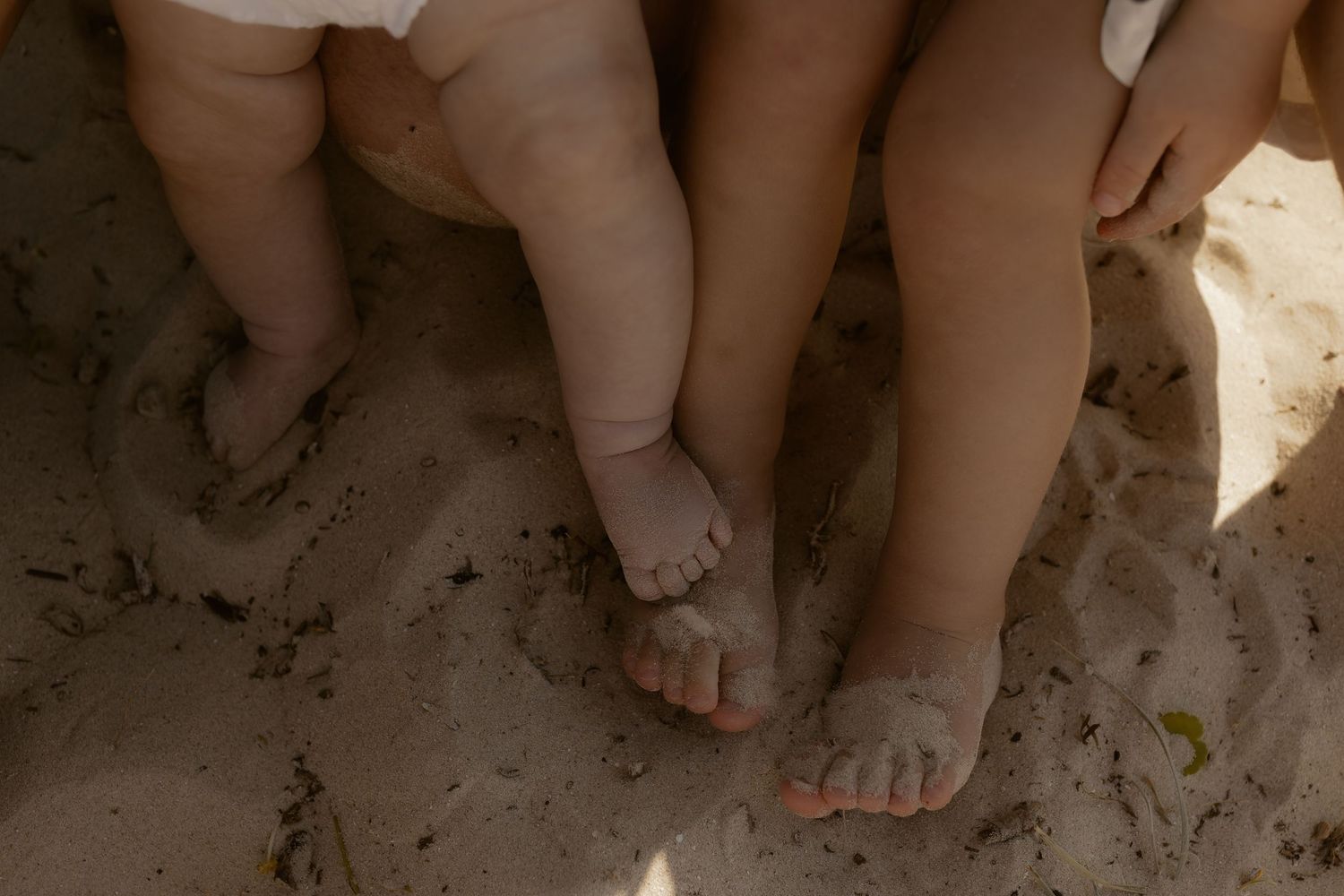 Close-up of bare feet in sand showing family connection and intimacy.
