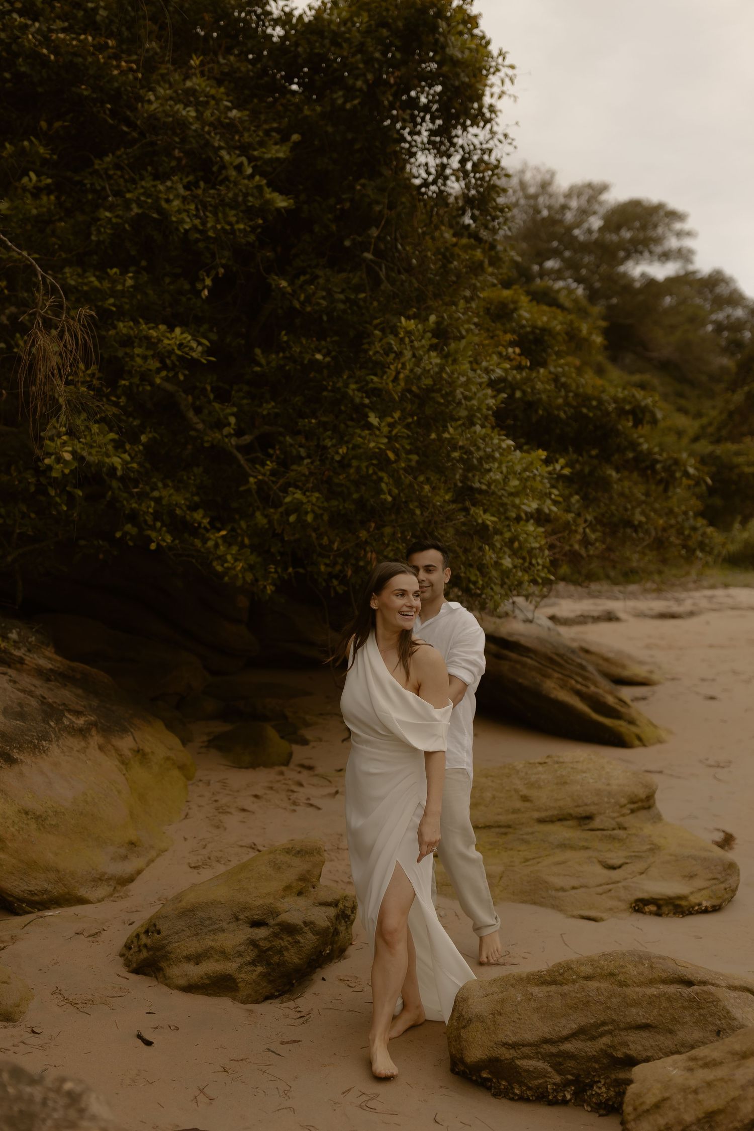 A romantic couple embraces on a rocky beach during a moody overcast day.