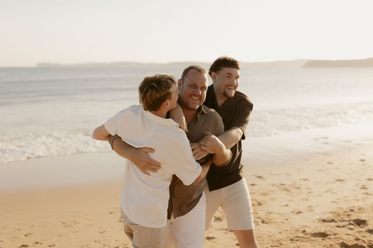 A couple embraces while standing on a sandy beach during sunset.