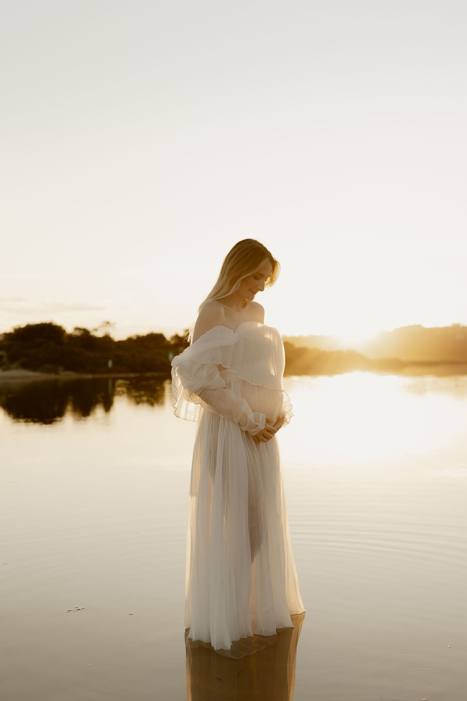 Figure in ethereal white dress stands peacefully in still waters during golden hour.