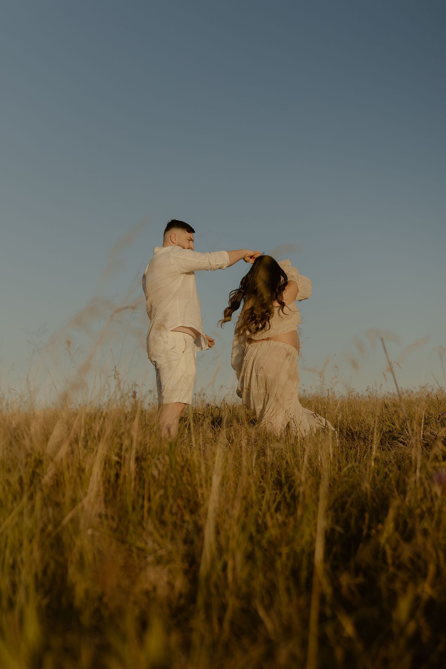 A couple dances together in a golden field at sunset with tall grass swaying around them.