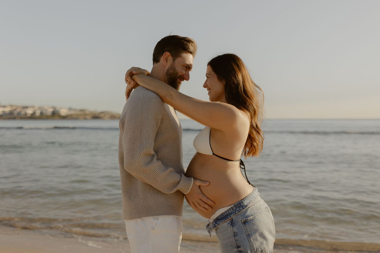 Couple shares tender moment during beach maternity photoshoot at sunset.