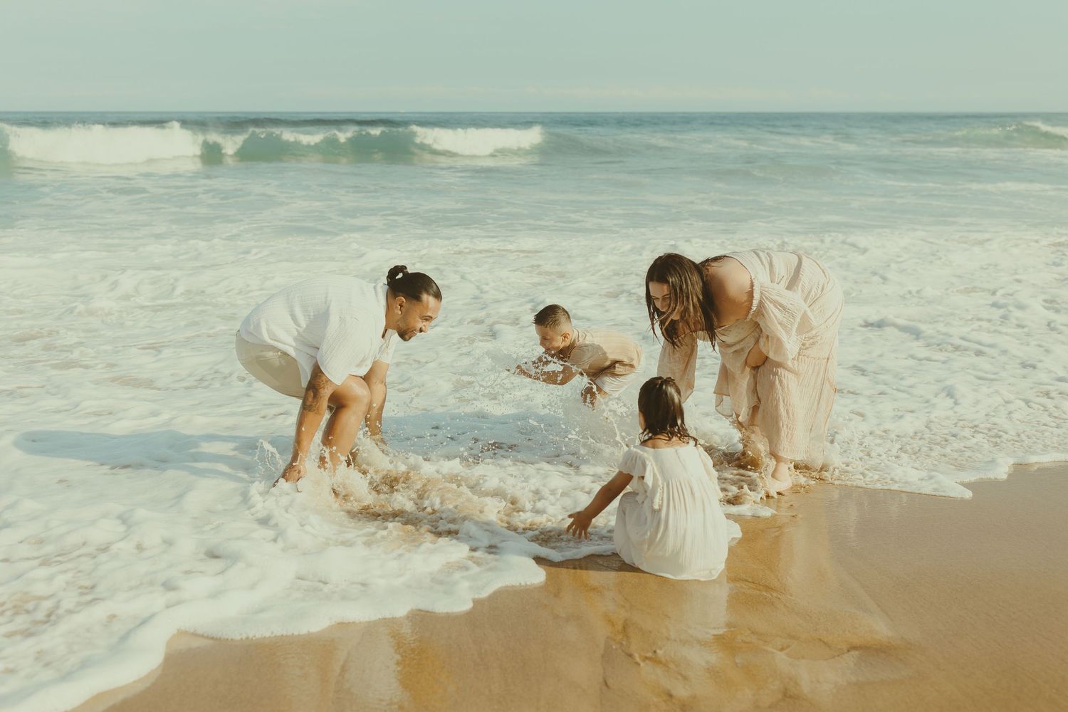 People playing and splashing in the ocean waves at a sandy beach during a sunny day.