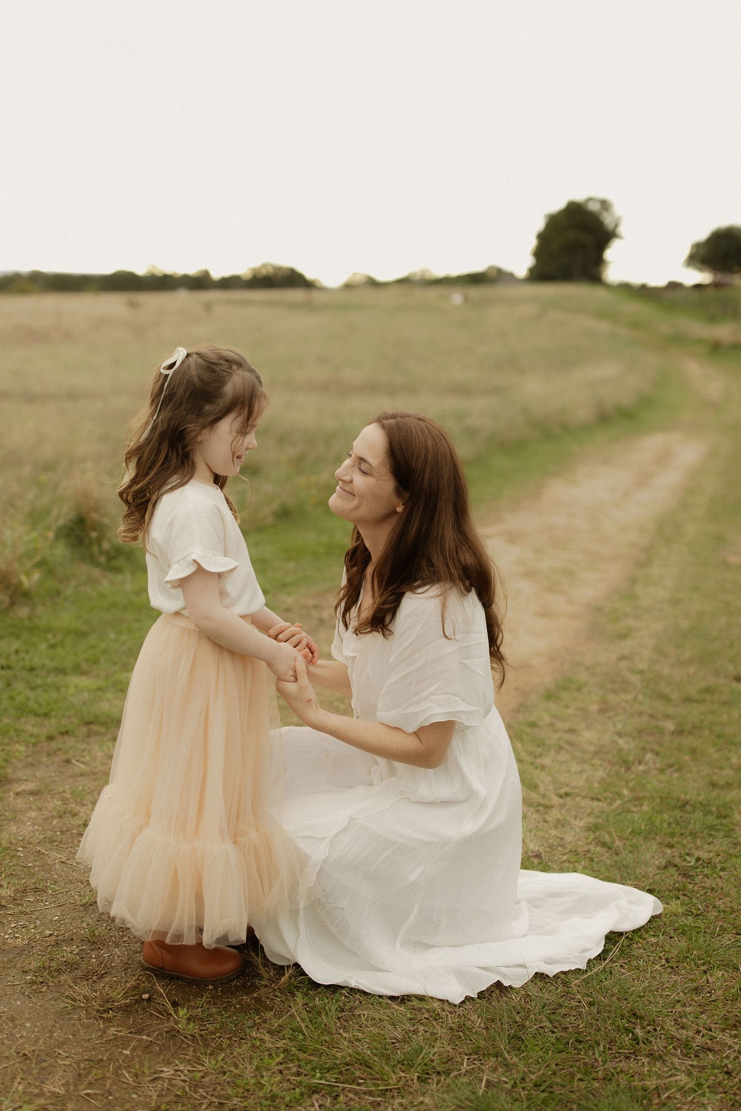 A tender moment between two people in white dresses on a grassy path during golden hour.