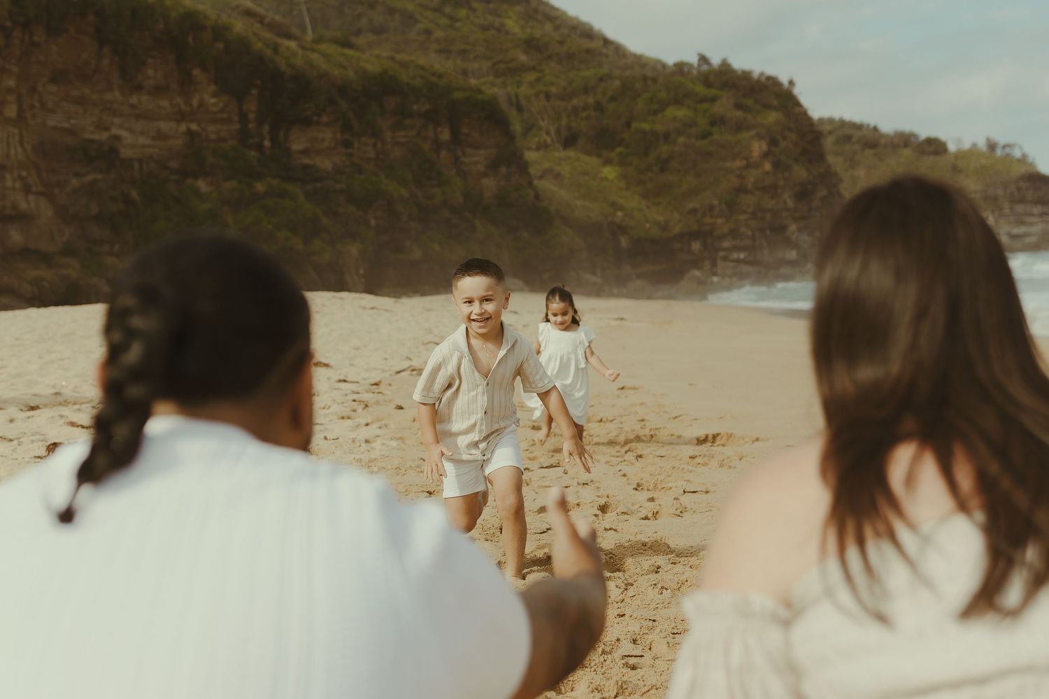 A group of people enjoy a sunny day at a sandy beach with cliffs in the background.