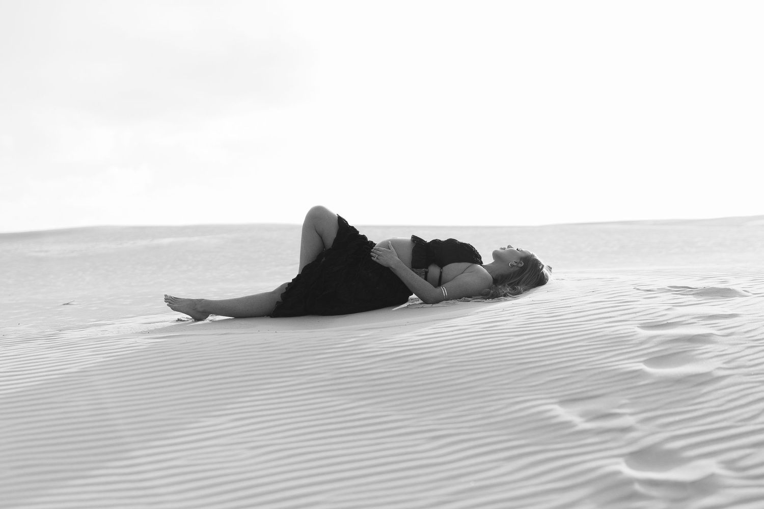 Silhouettes of a person and horse create dramatic shadows on rolling sand dunes in monochrome.