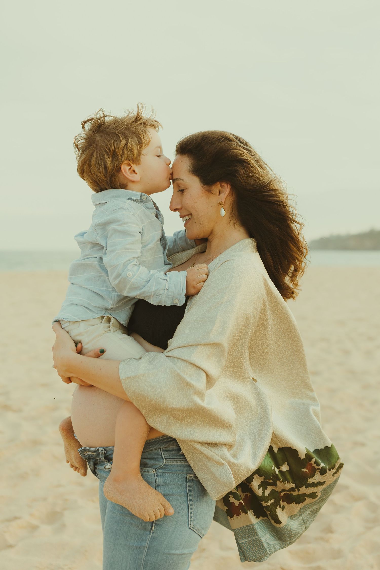 Tender moment between parent and child embracing on a peaceful beach at sunset.