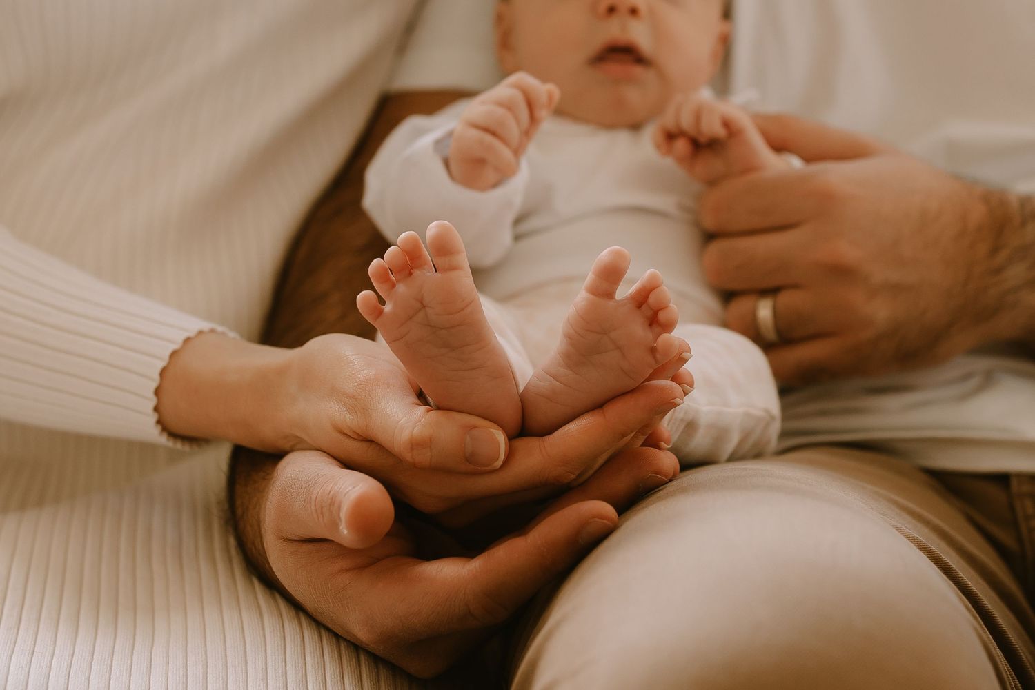 Close up of tiny baby feet being held in gentle adult hands against soft white bedding.