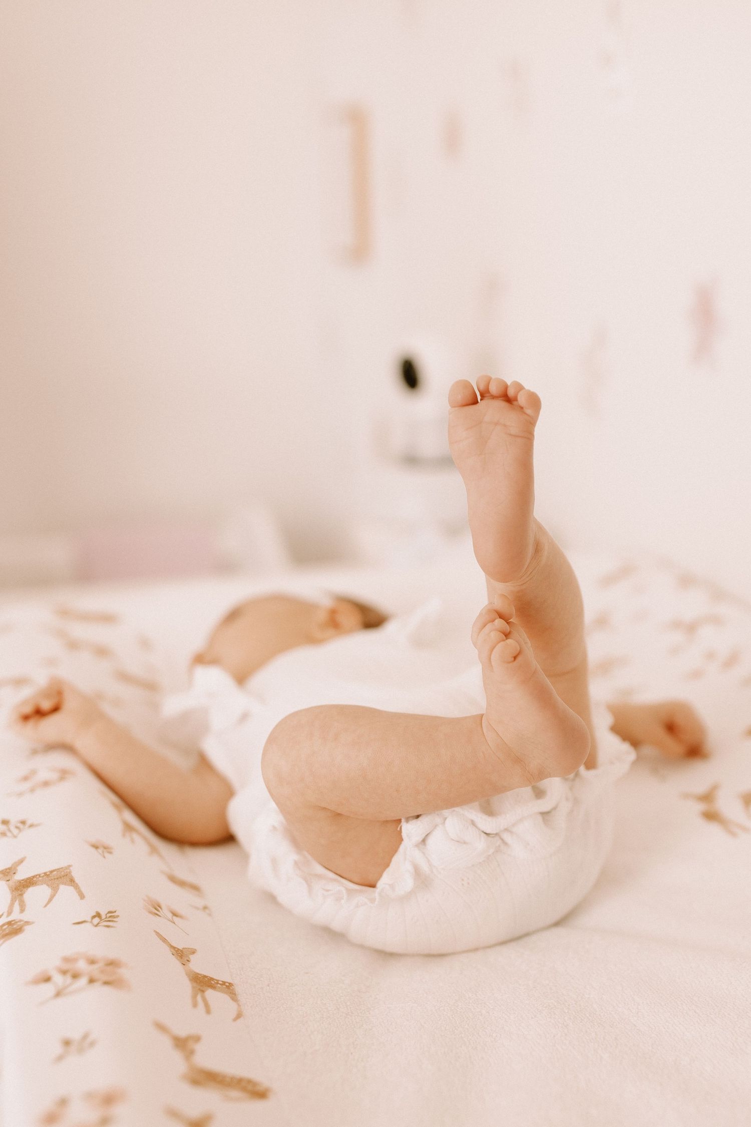 A tiny baby foot sticks up from soft white bedding with giraffe print details.