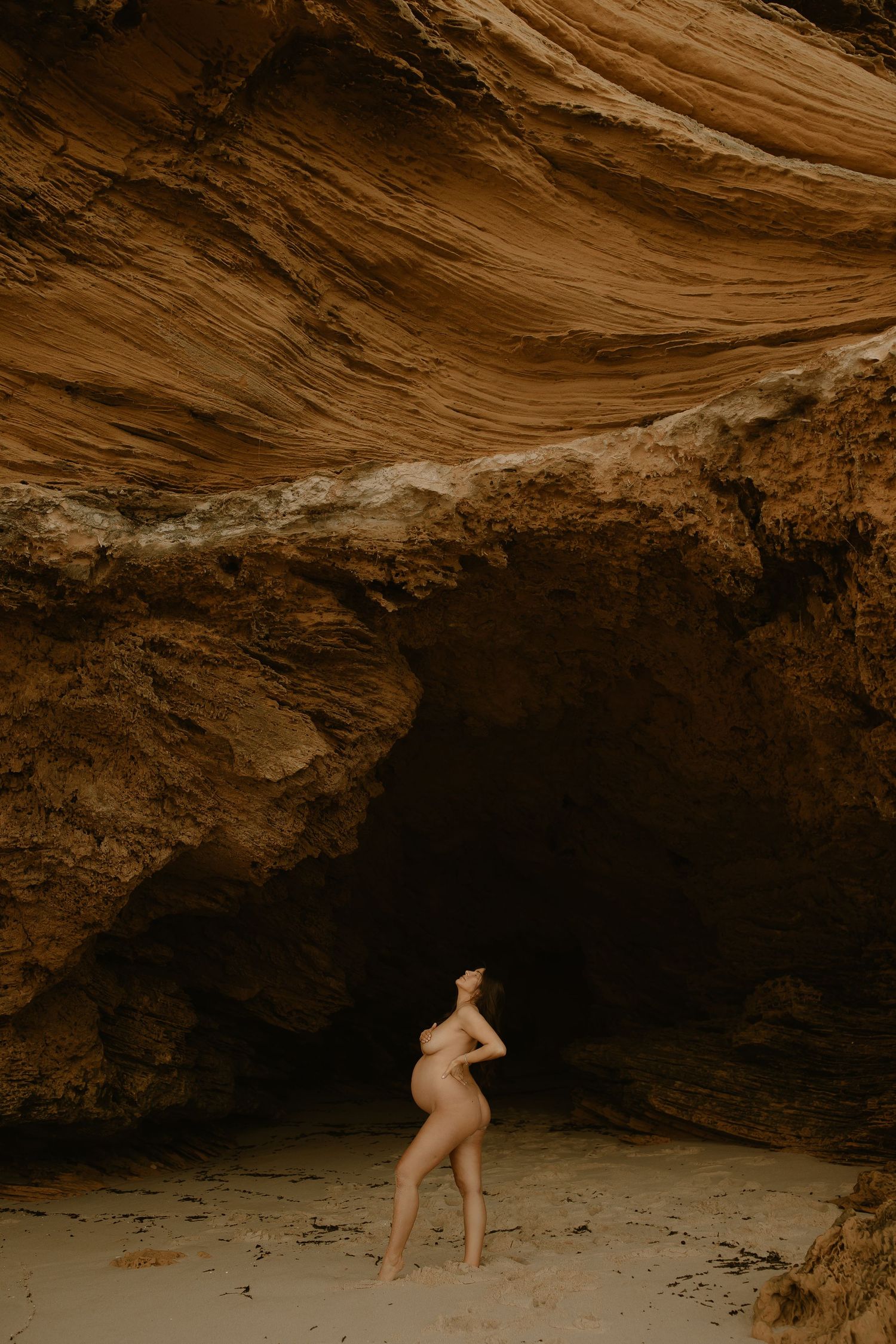 Silhouette figure standing in natural cave entrance with dramatic rocky overhang in sepia tones.