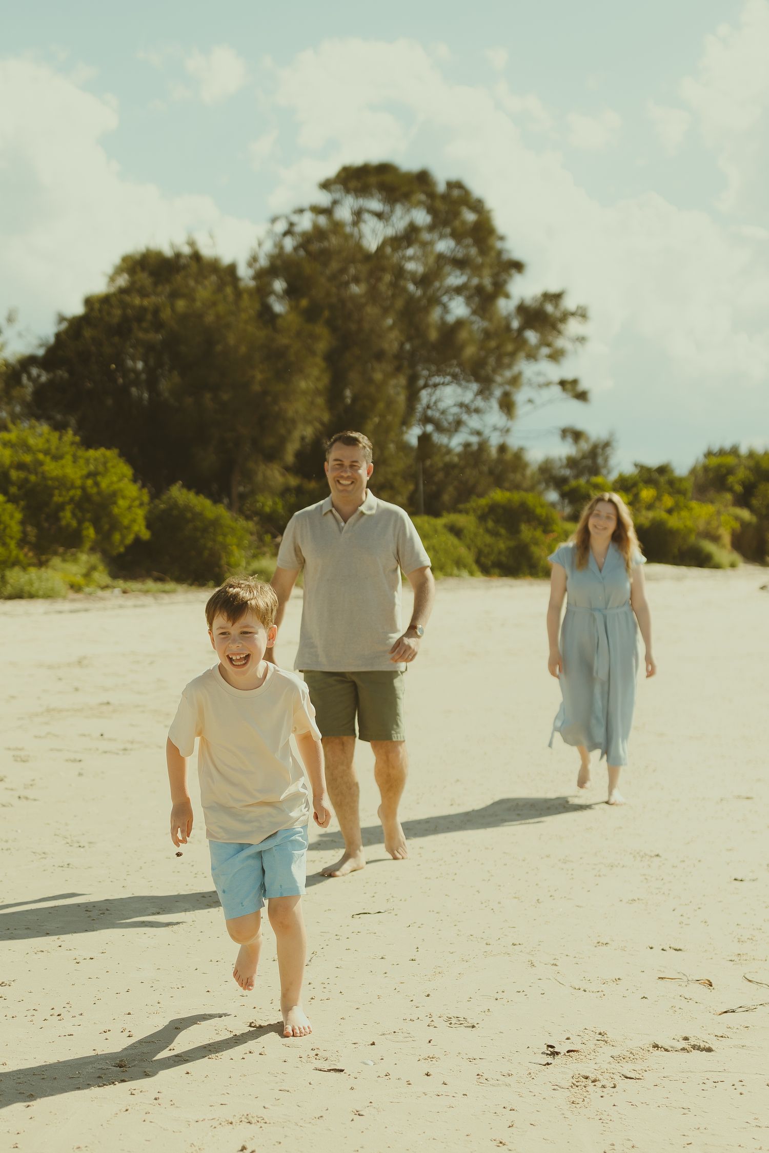 A family walks together on a pristine white sandy beach on a sunny summer day, casting long shadows behind them.