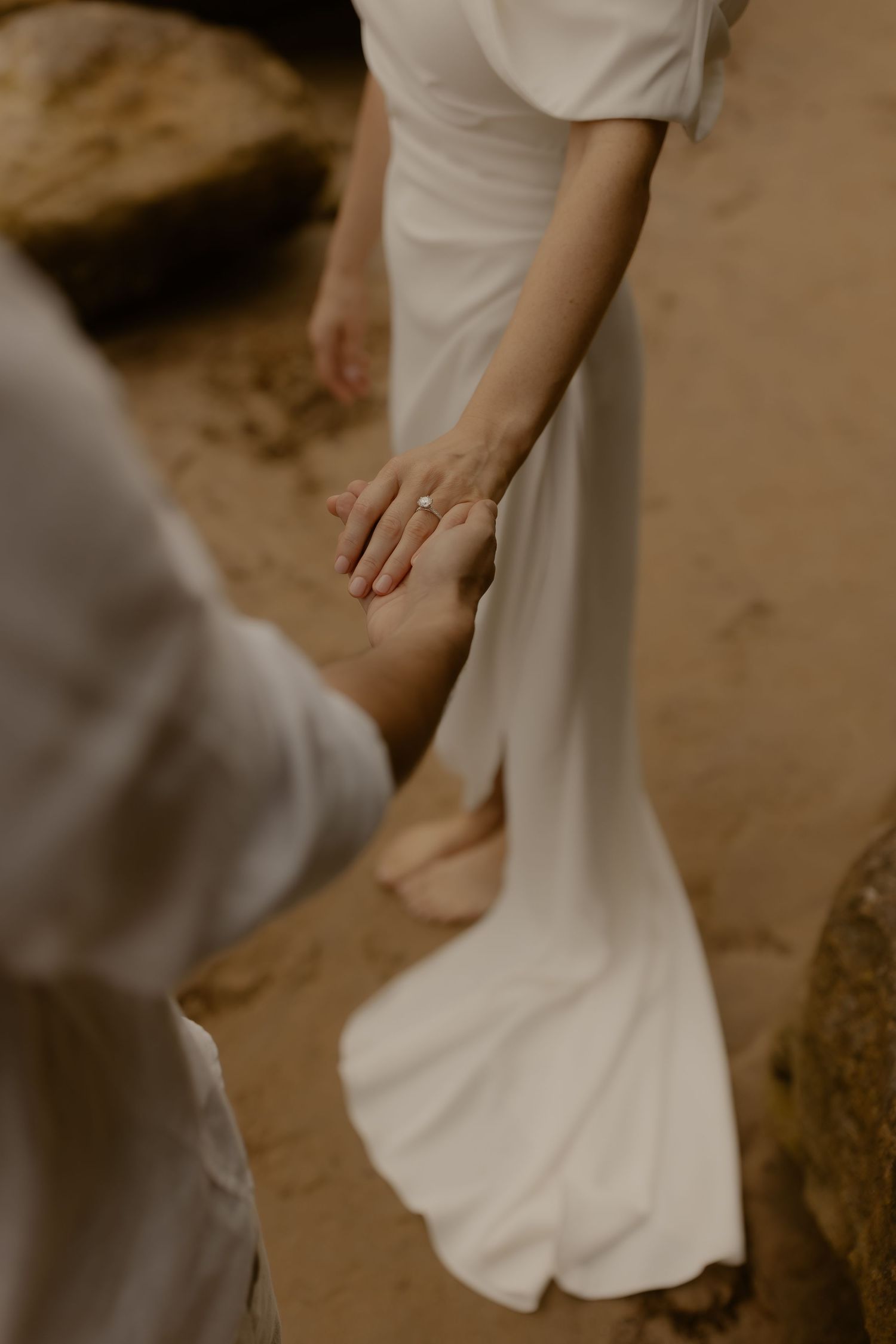 White flowing wedding dress detail against sandy beach backdrop in warm sepia tones.