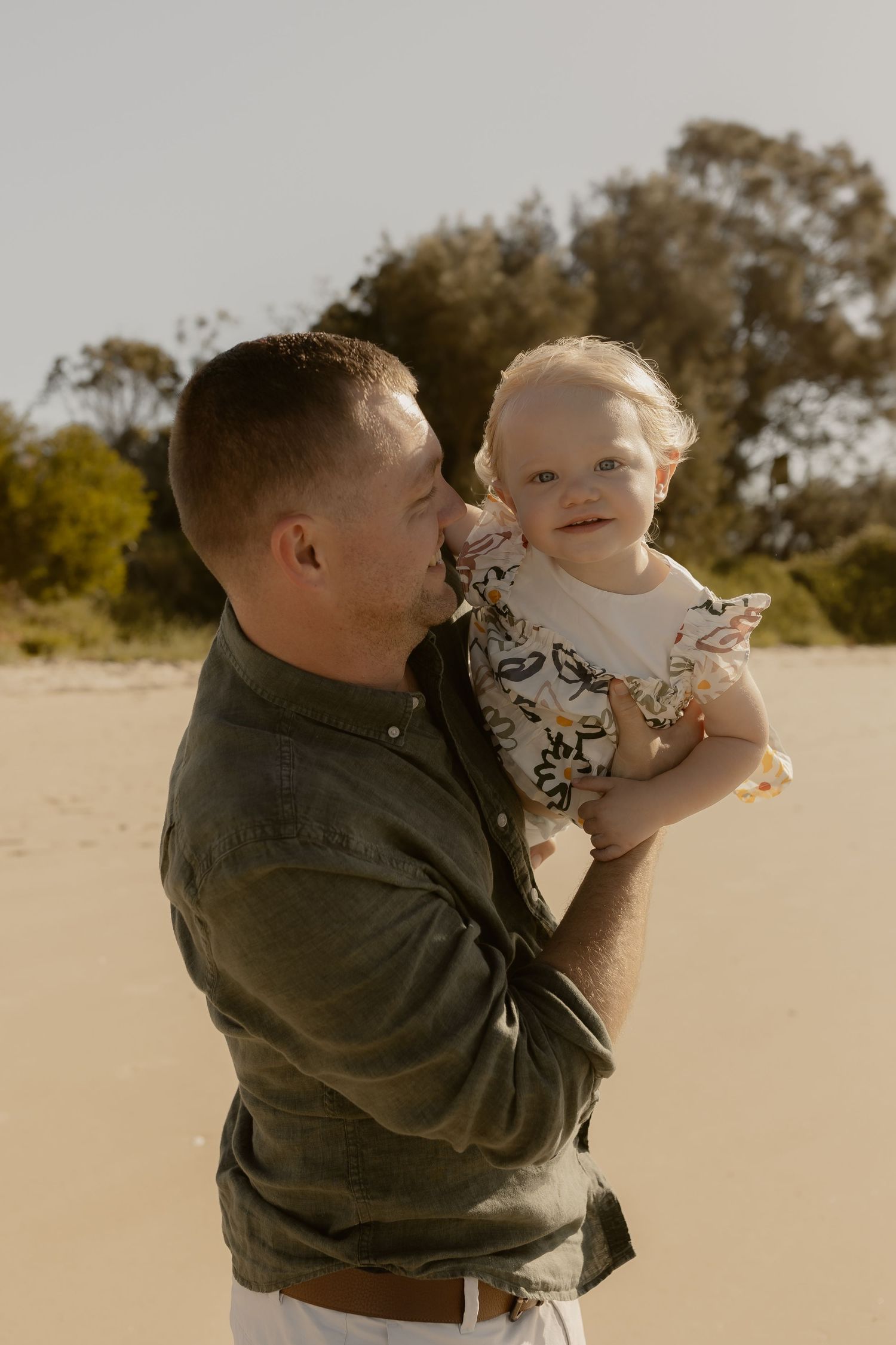 Adult holding and playing with small child on sandy beach during golden hour.