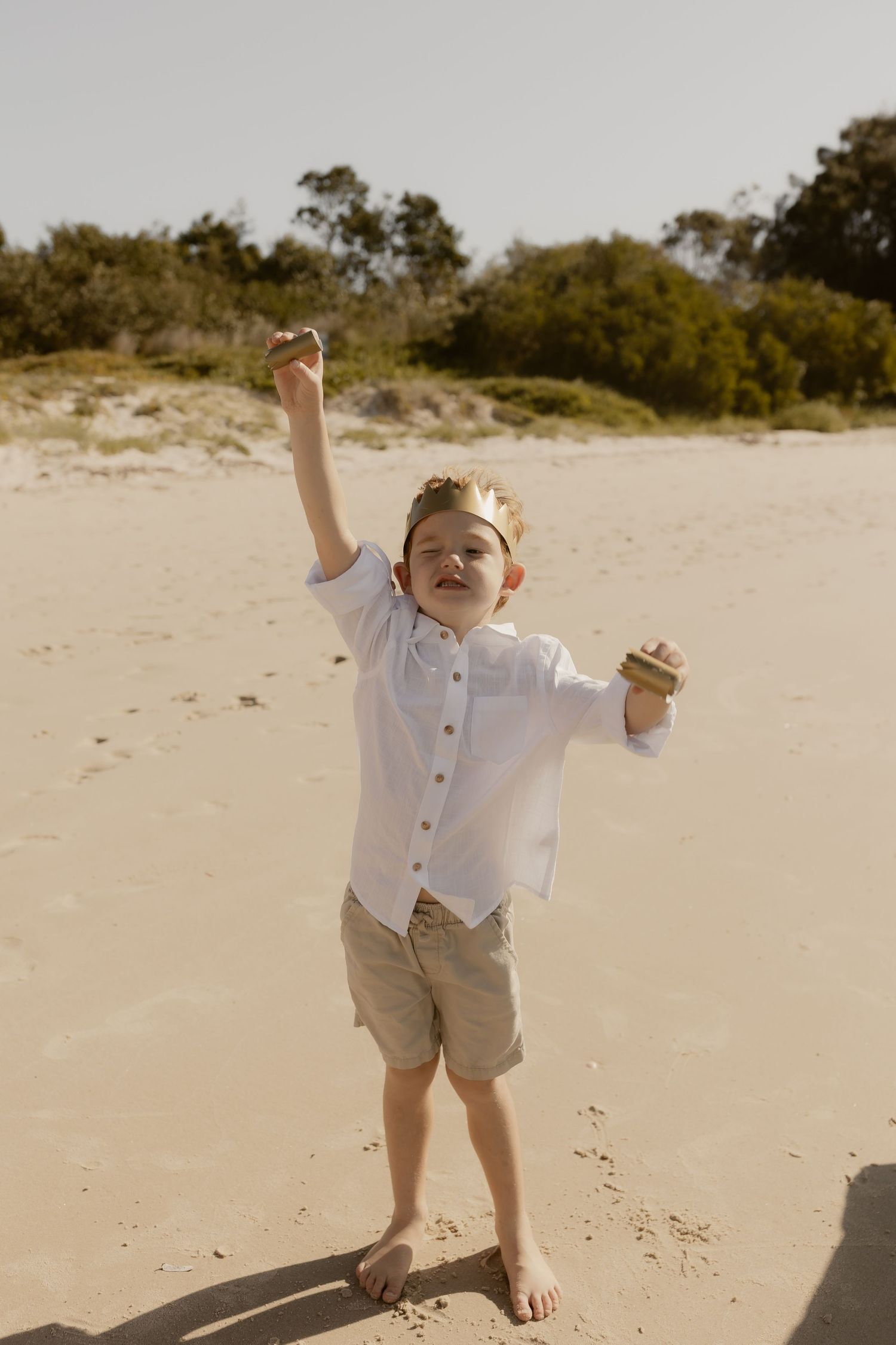 Child playing and expressing joy on a sunny beach in casual attire.