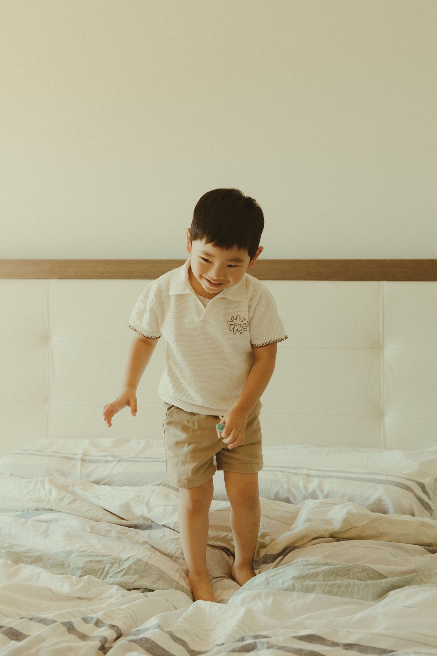 Child plays and jumps on unmade bed with white linens.