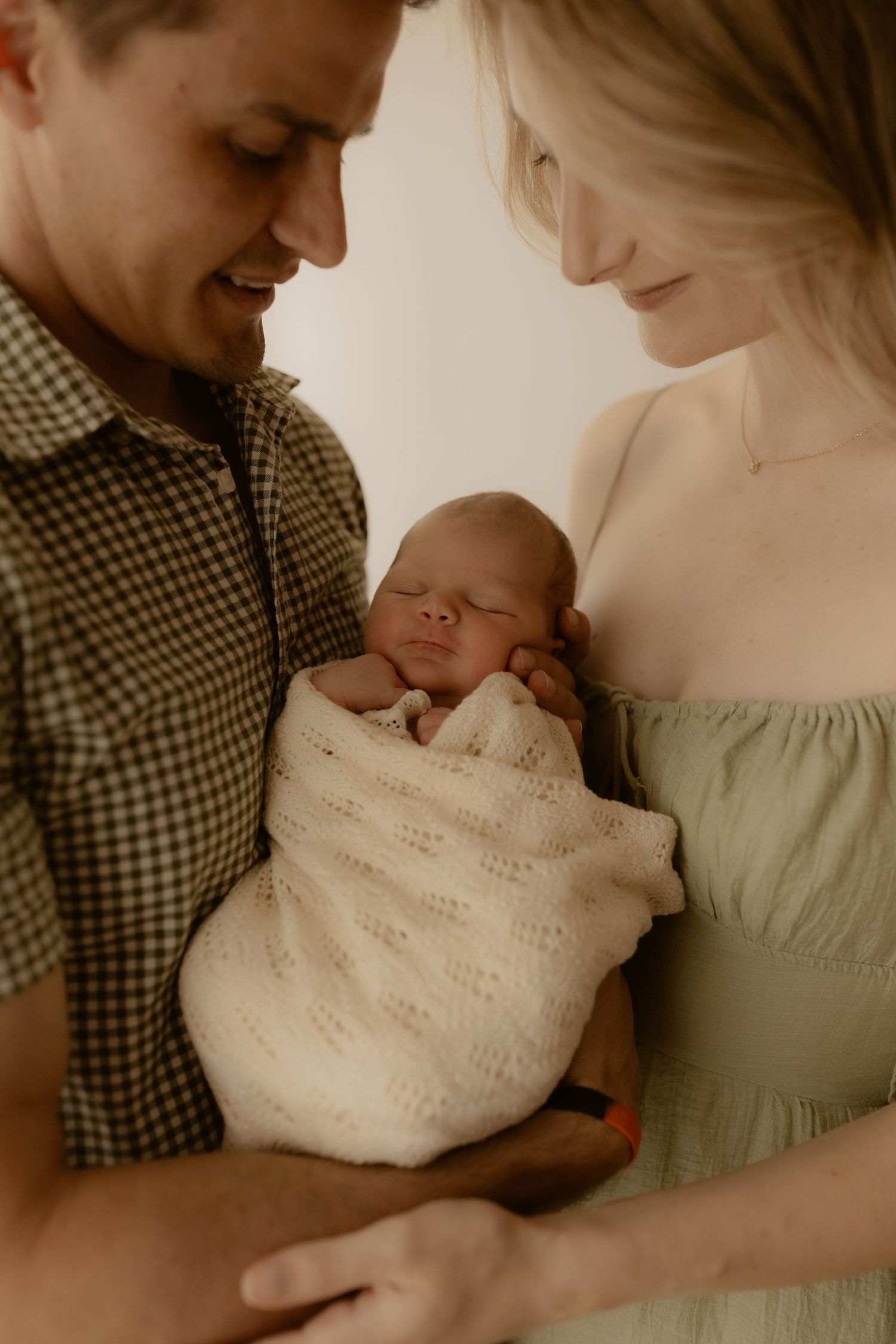 Parents sharing an intimate moment with their newborn baby in muted tones.