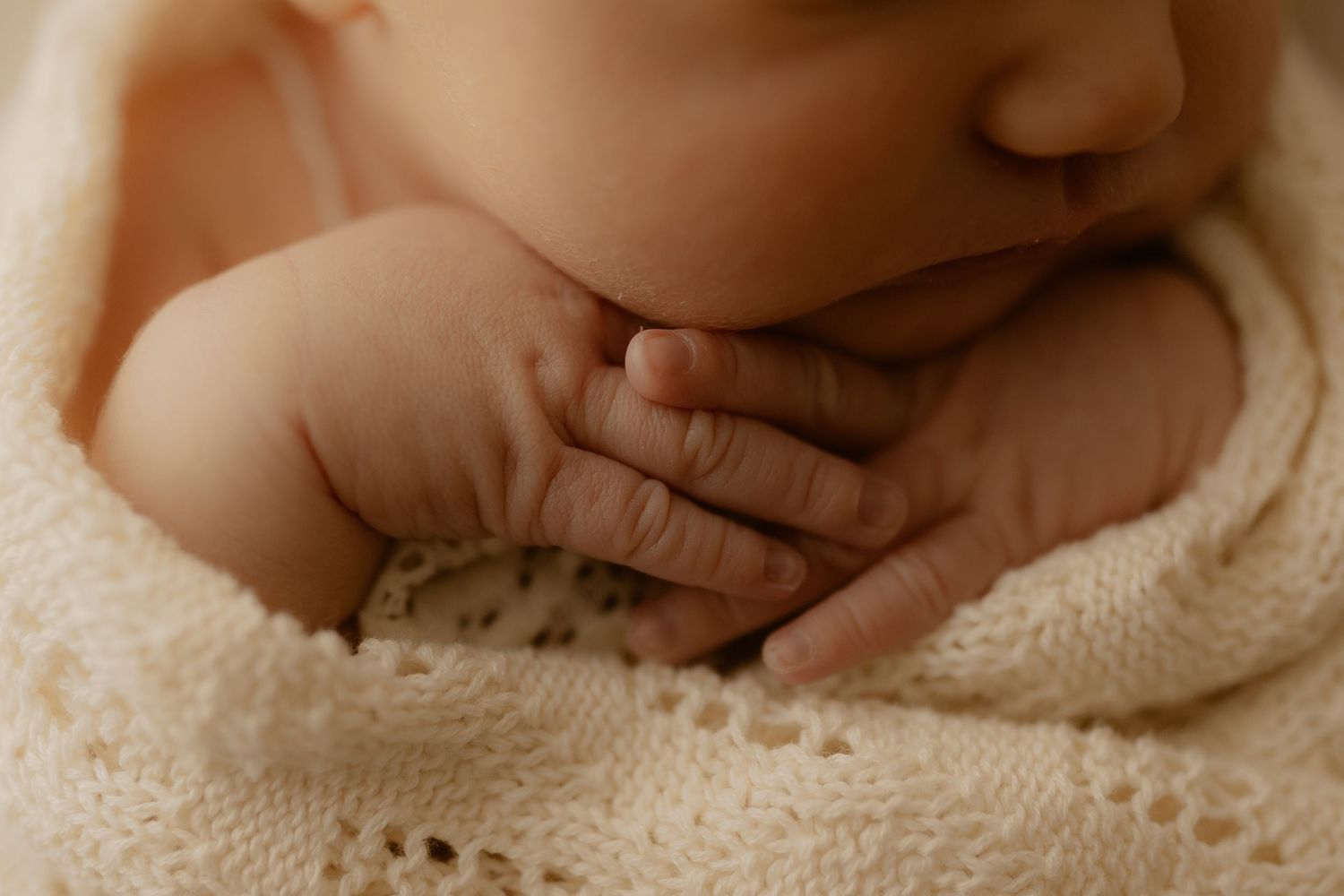 Close-up photo of a newborn baby's tiny fingers wrapped in soft white knitted fabric.